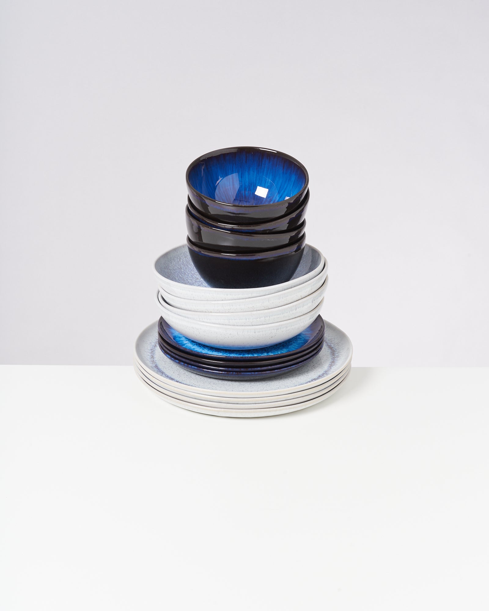 Gestapelte Keramikschalen und -teller in Blau- und Grautönen auf weißem Hintergrund.