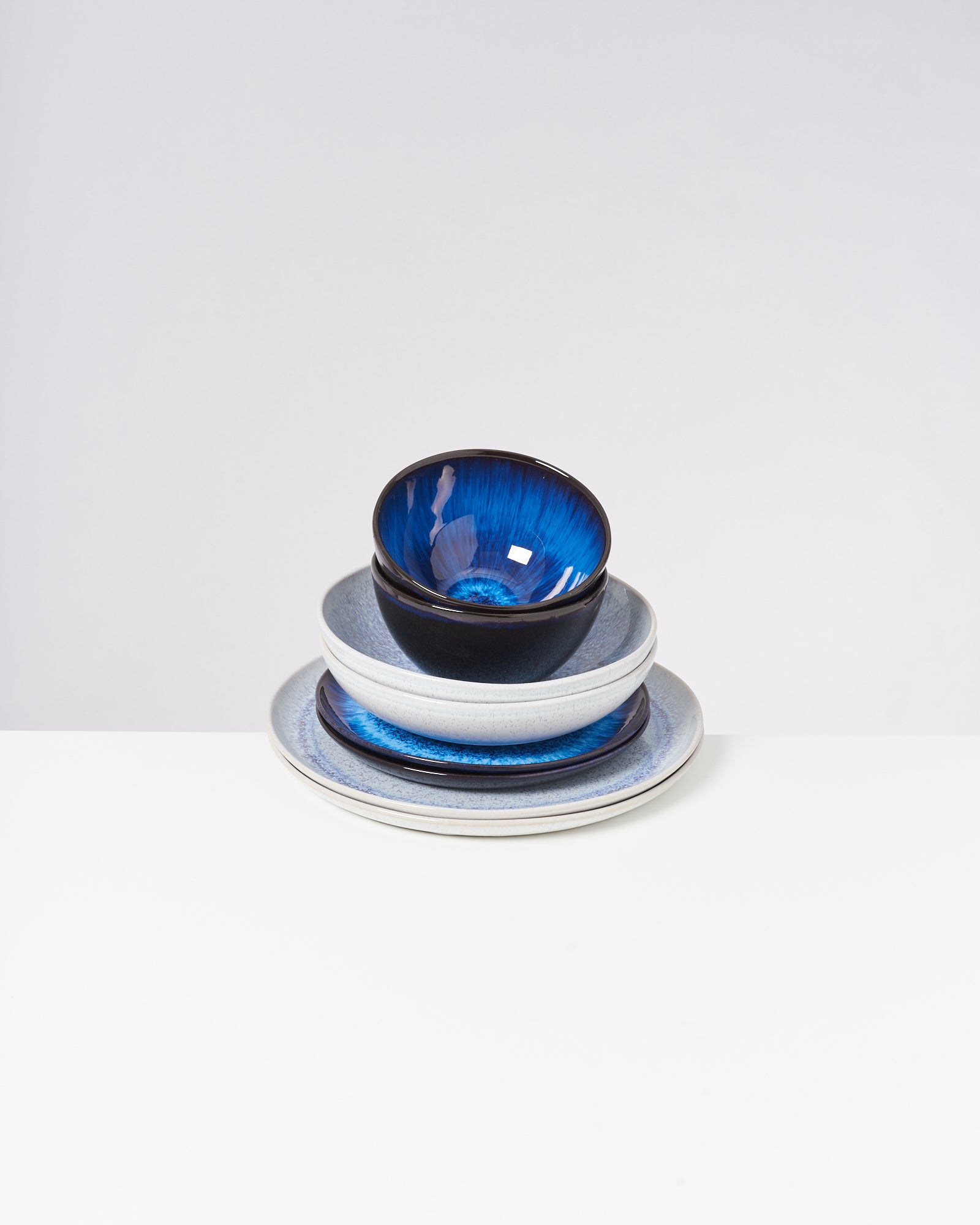 Ein Stapel aus Schüsseln und Tellern, bei denen die obere Schüssel innen blau ist, auf einem weißen Hintergrund.