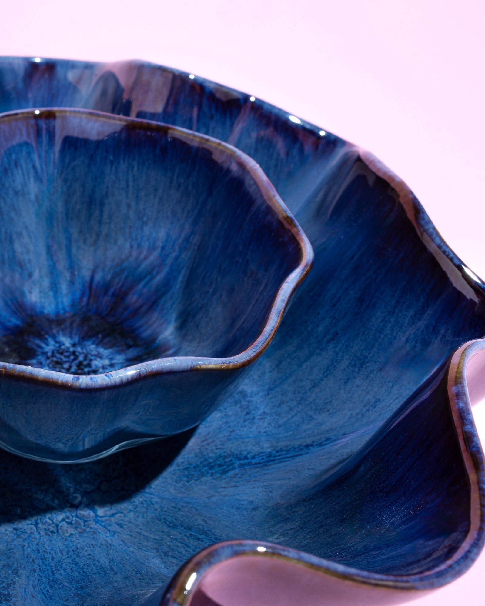 Nahaufnahme einer blau glasierten, wellenförmigen Keramikschale auf rosa Hintergrund.