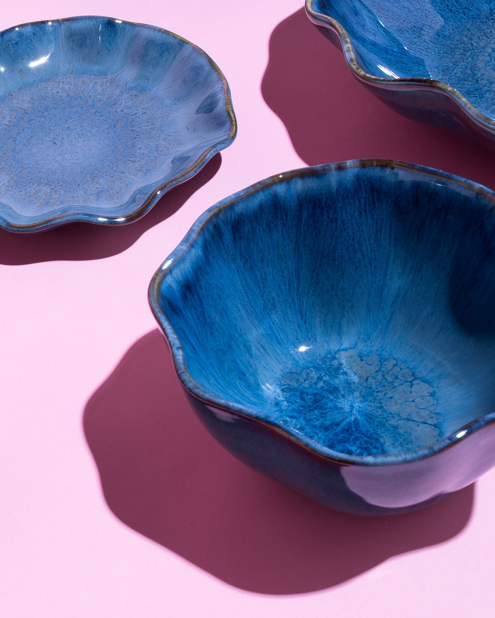 Drei blaue Keramikschalen auf rosa Hintergrund, die Schatten werfen.