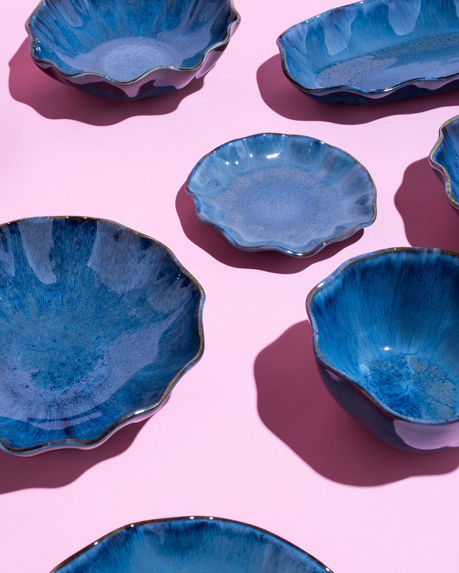 Blaue, wellige Keramikteller und Schalen auf rosa Hintergrund, von oben fotografiert.