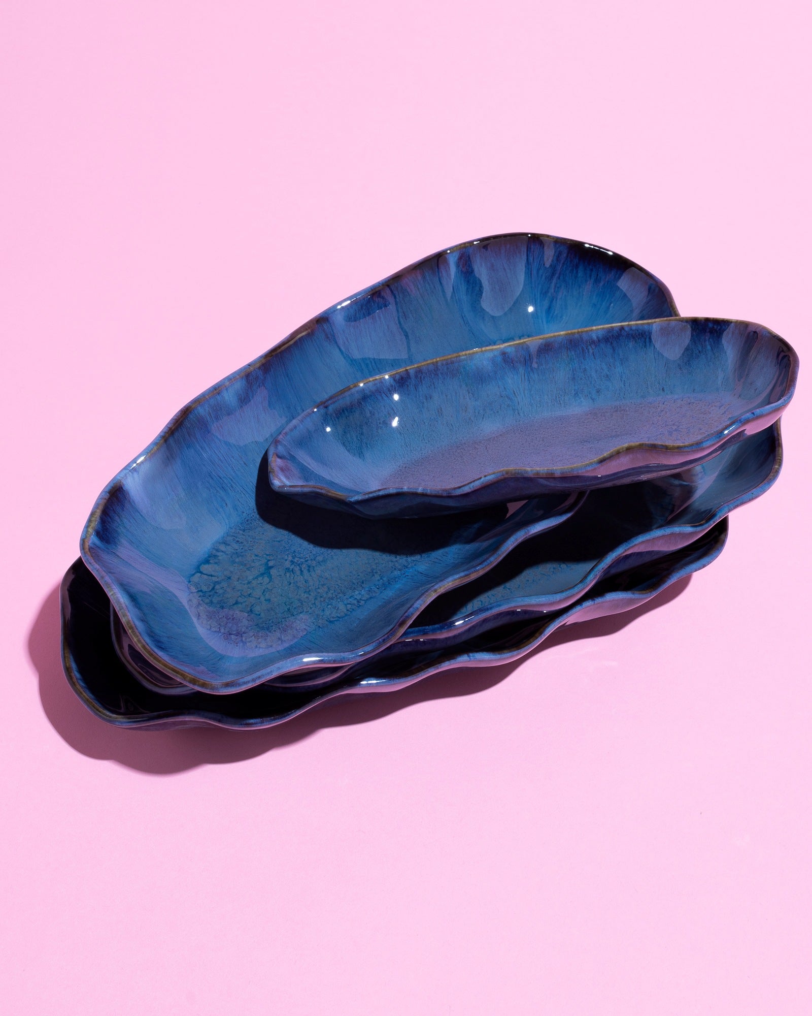 Stapel blauer, wellenförmiger Keramikteller auf rosa Hintergrund.