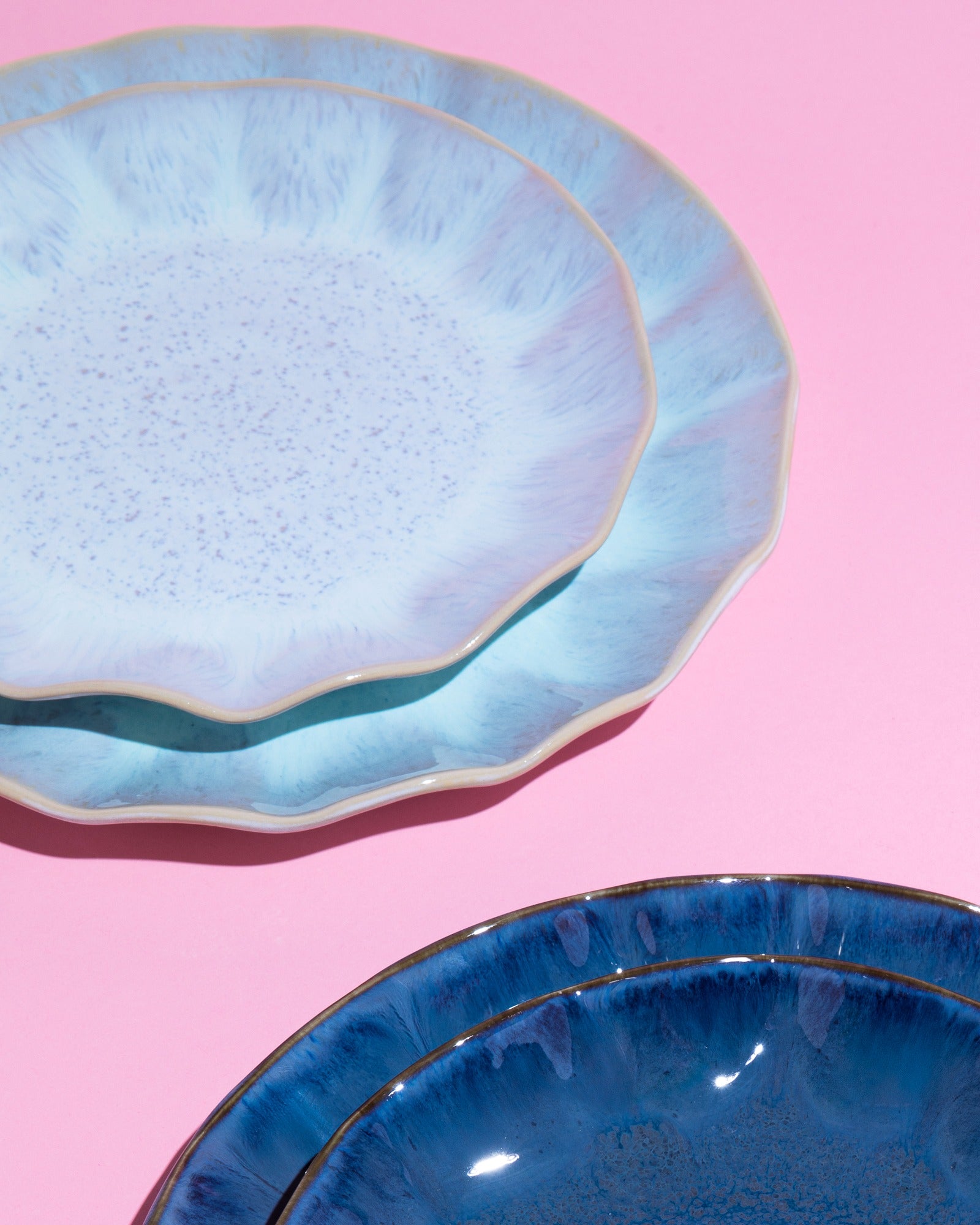 Drei blau glasierte Teller auf einem rosa Hintergrund gestapelt.