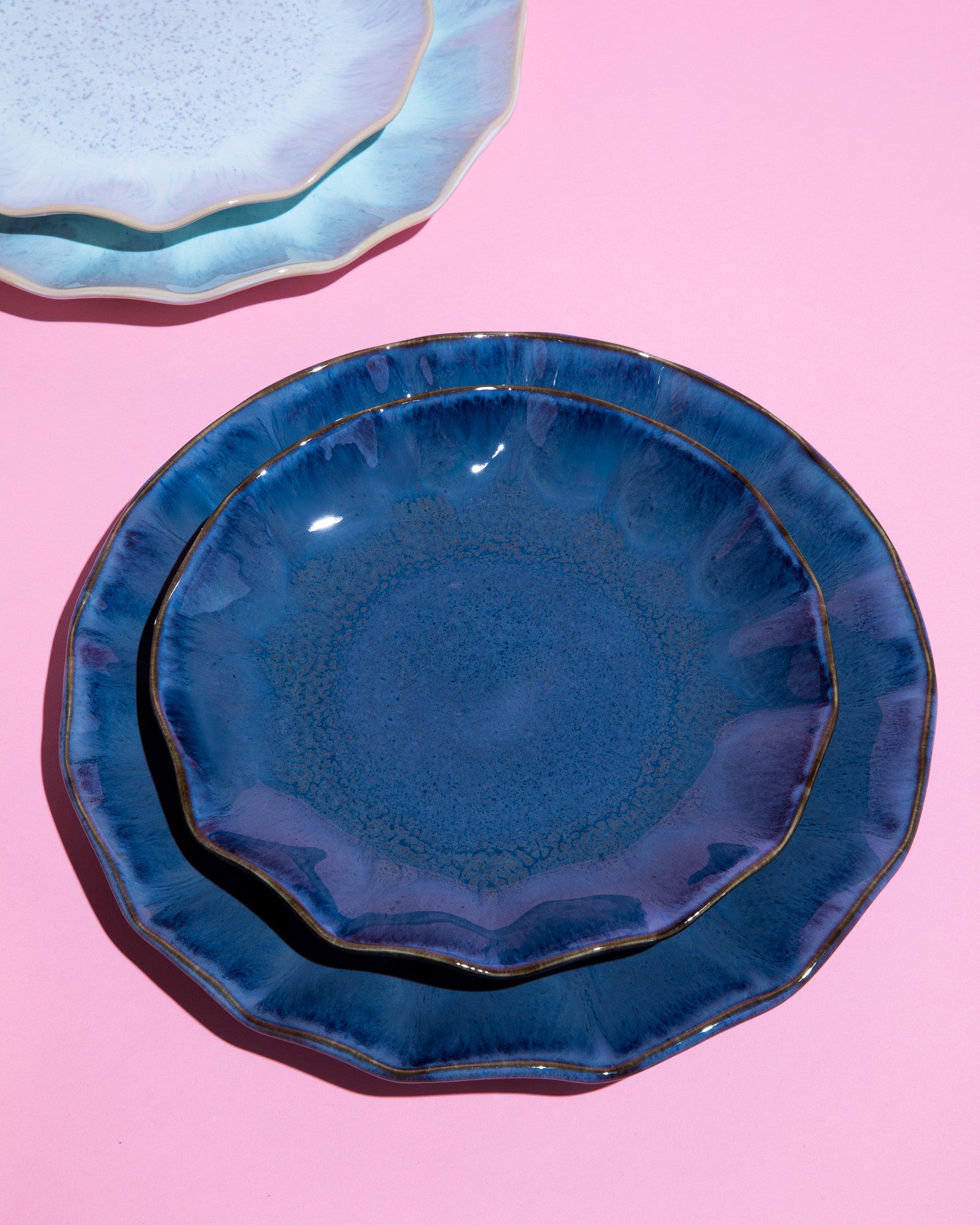 Zwei blaue Keramikteller auf einem pinken Hintergrund, mit zusätzlichen hellblauen Tellern im Hintergrund.