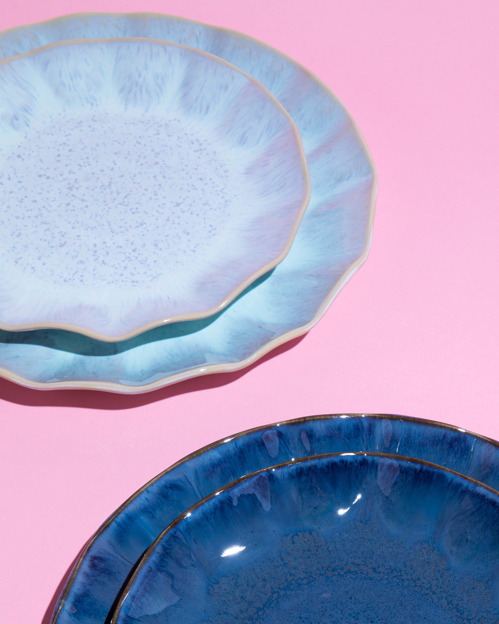 Zwei Stapel blauer Keramikteller auf einem rosa Hintergrund.