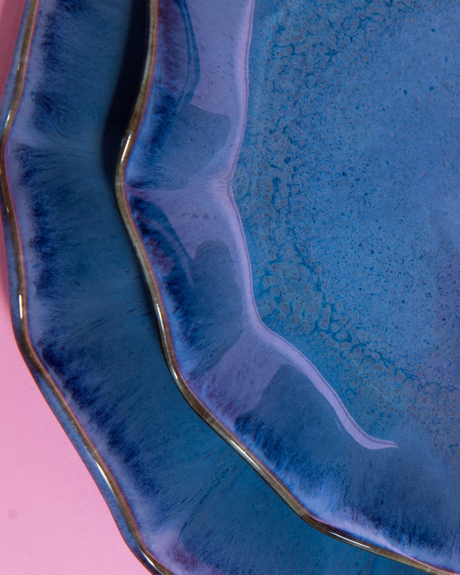 Zwei überlappende, blaue Keramikteller mit unregelmäßigen Rändern auf einem rosa Hintergrund.