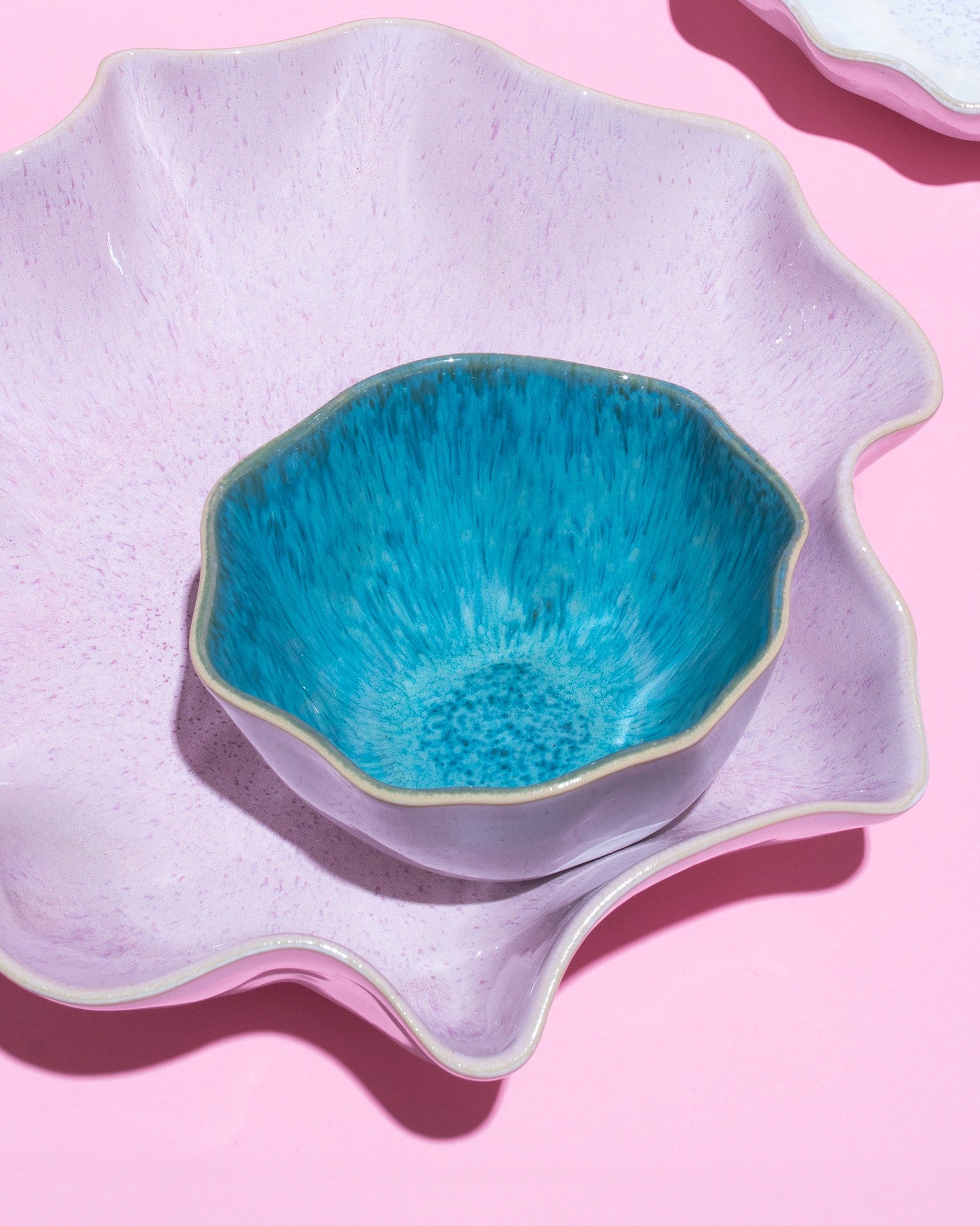 Zwei dekorative Schalen, eine in Türkis und die andere in Lila, auf einem rosa Hintergrund.