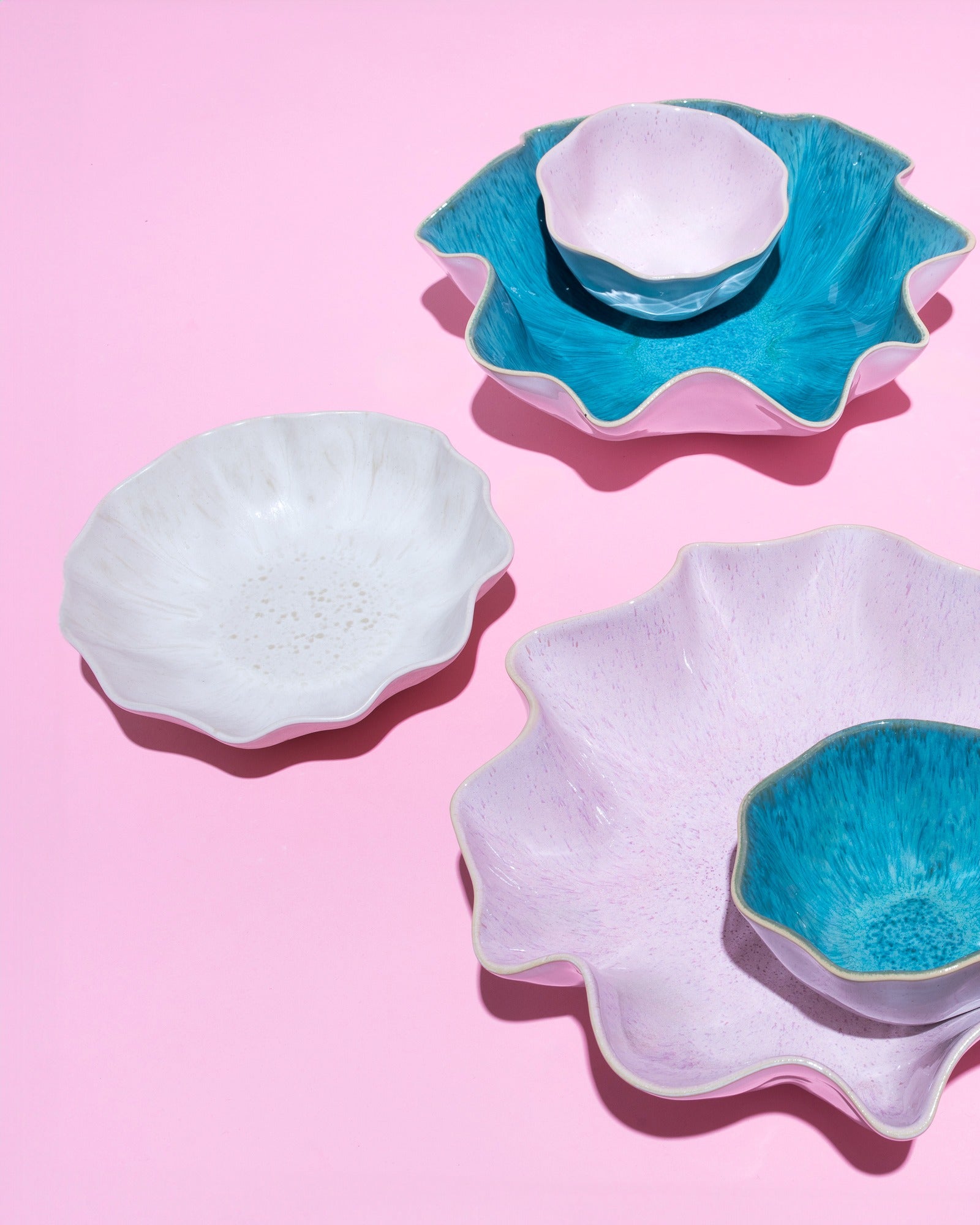 Verschiedene Schalen mit gewellten Rändern in Blau, Weiß und Rosa auf einem rosa Hintergrund.