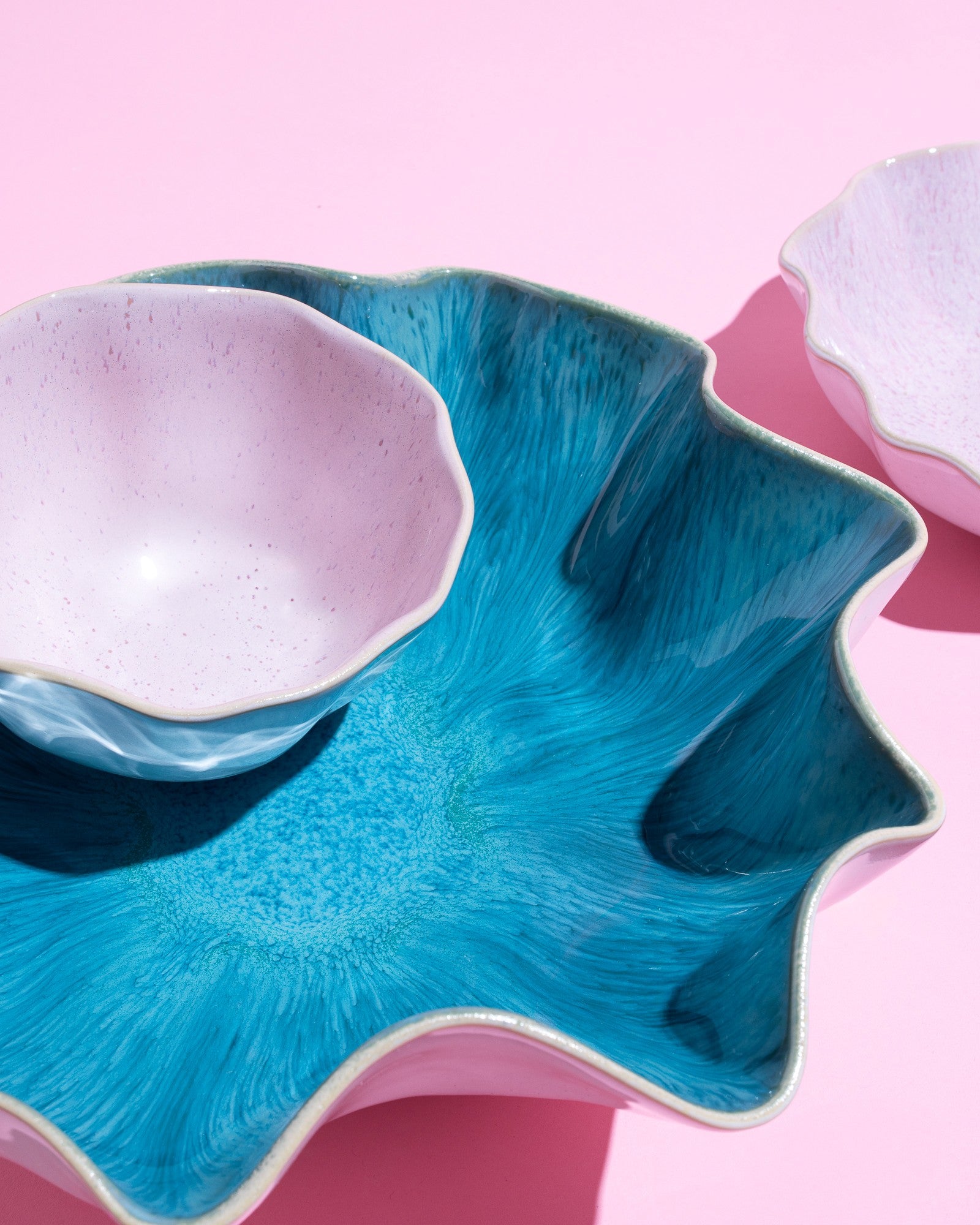 Zwei dekorative Keramikschalen, eine blau, die andere rosa, auf einem rosa Hintergrund.