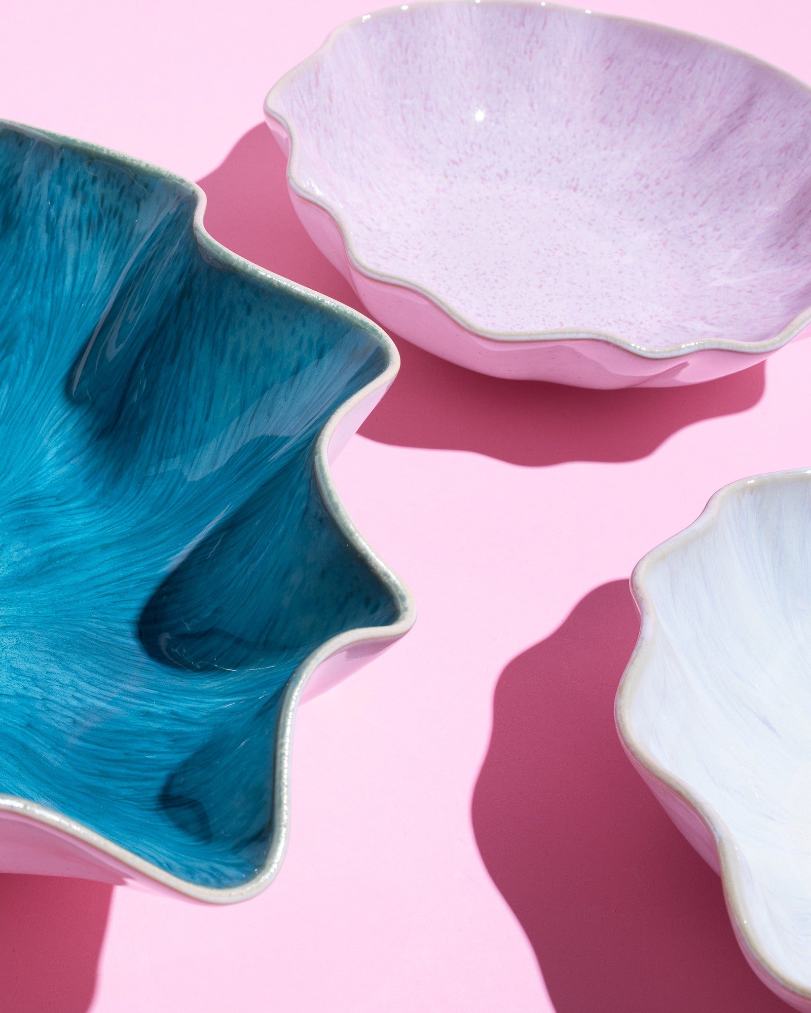 Drei gewellte Schalen in Blau, Rosa und Weiß auf einem rosa Hintergrund.