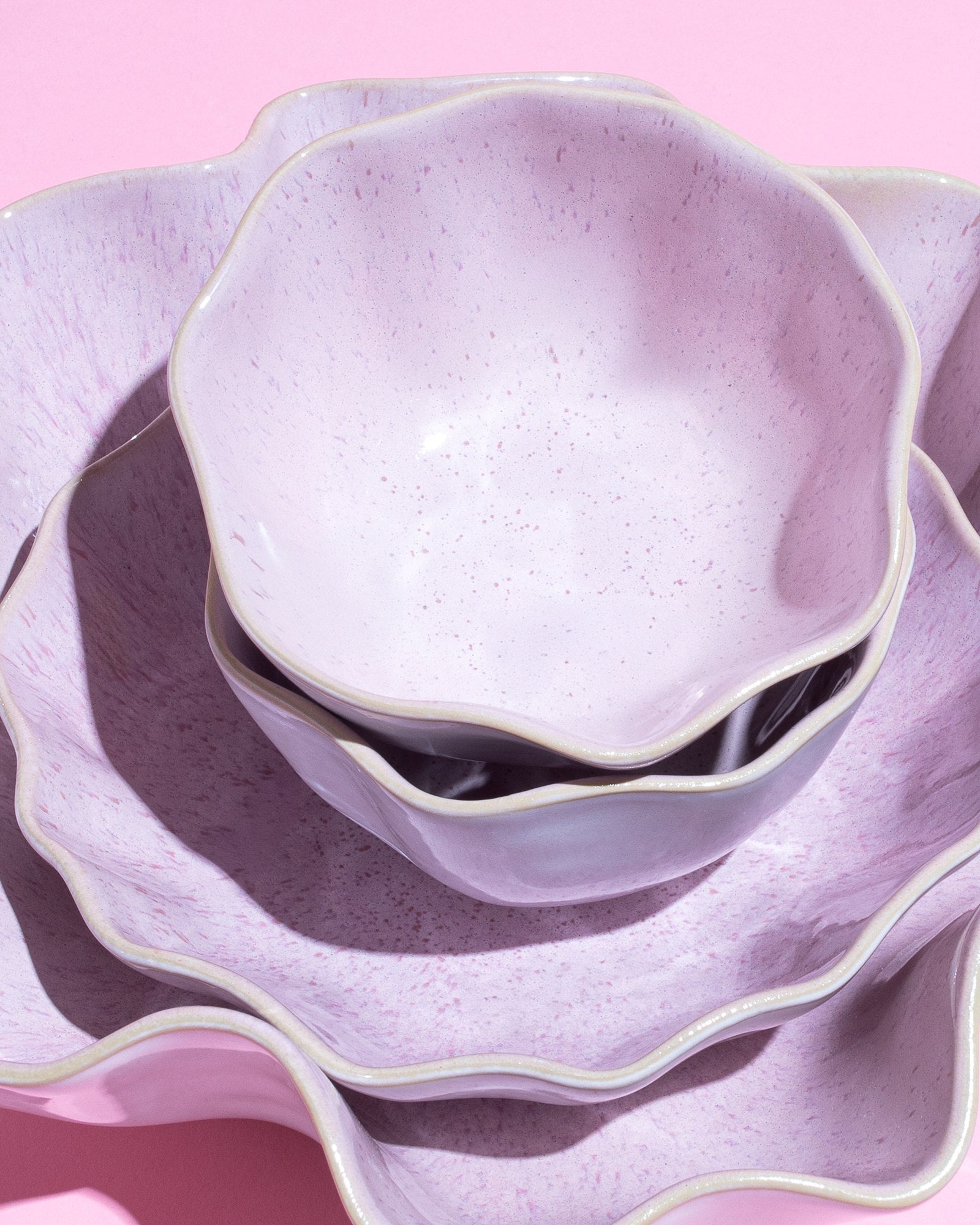 Verschachtelte, wellenförmige Pastellviolette Schalen auf rosa Hintergrund.