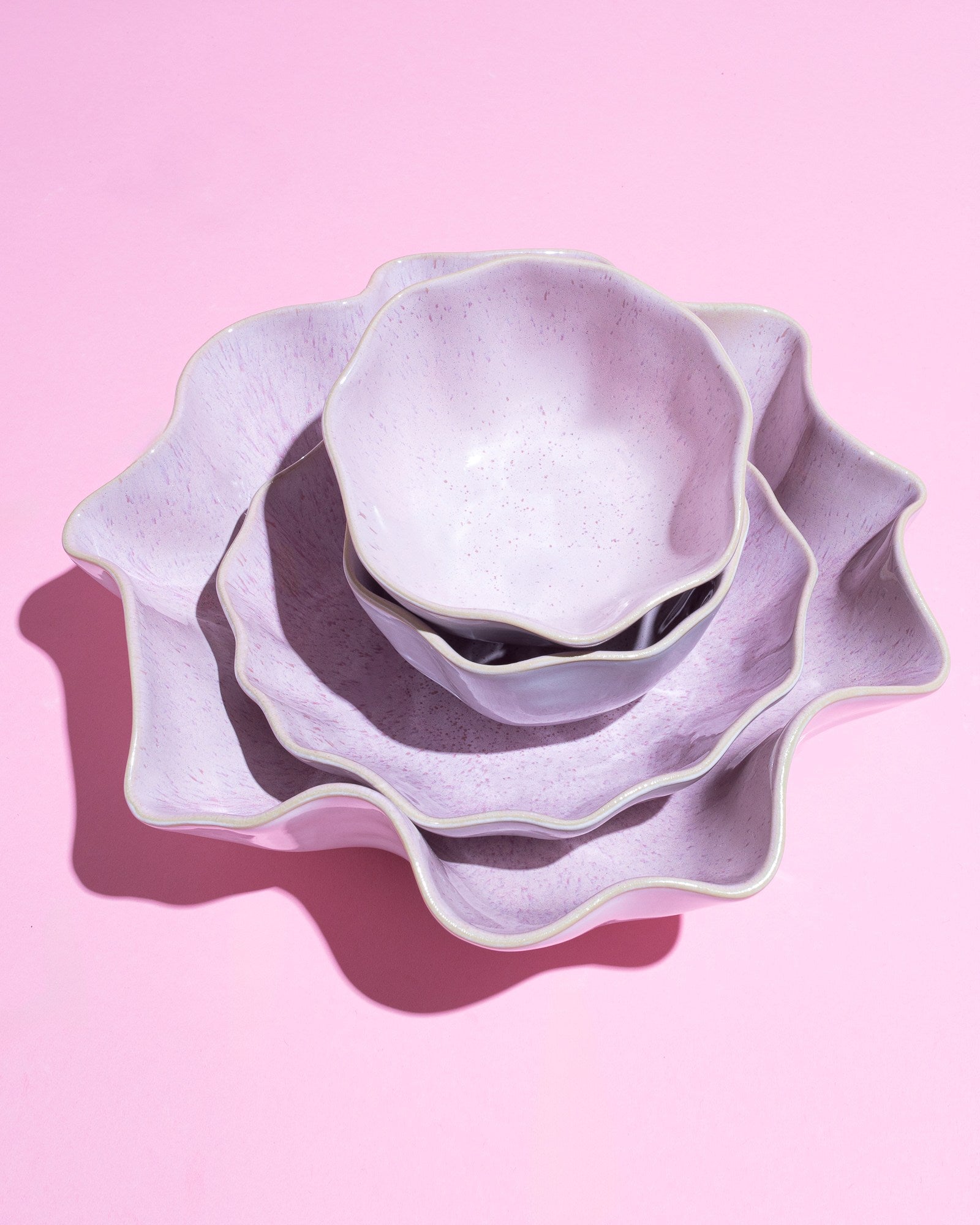Drei lila, wellenförmige Schüsseln sind ineinander gestapelt auf einem rosa Hintergrund.