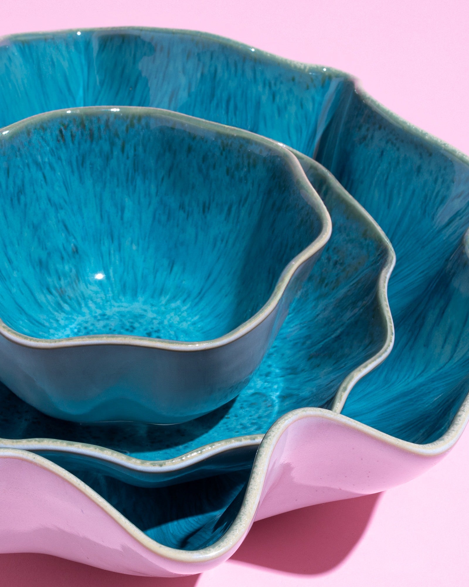 Blau und rosa gefärbte, ineinander gestapelte Keramikschalen mit welligem Rand auf rosa Hintergrund.