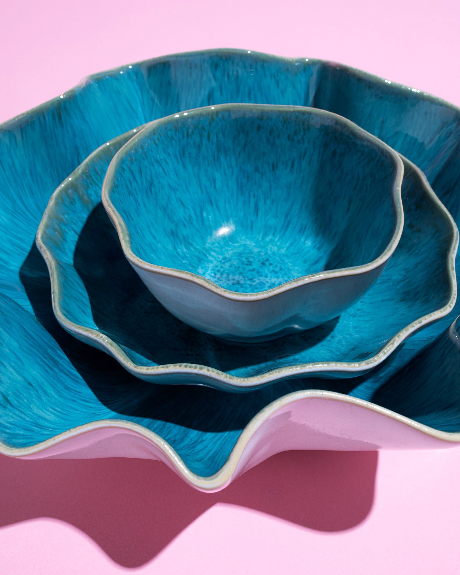 Drei ineinander gestapelte, blaugefärbte Keramikschalen auf einem rosa Hintergrund.
