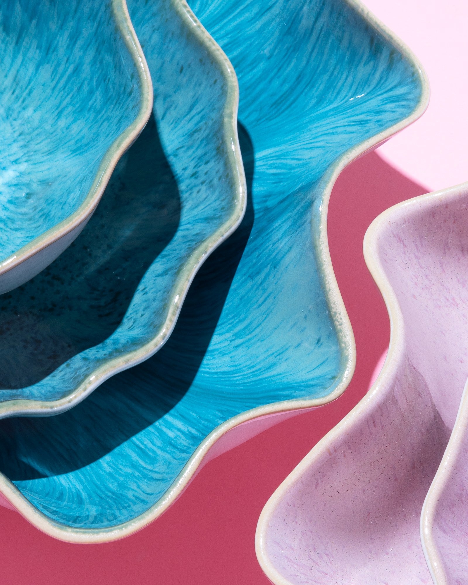 Blau- und rosafarbene, wellenförmige Keramikschalen auf rosa Hintergrund.