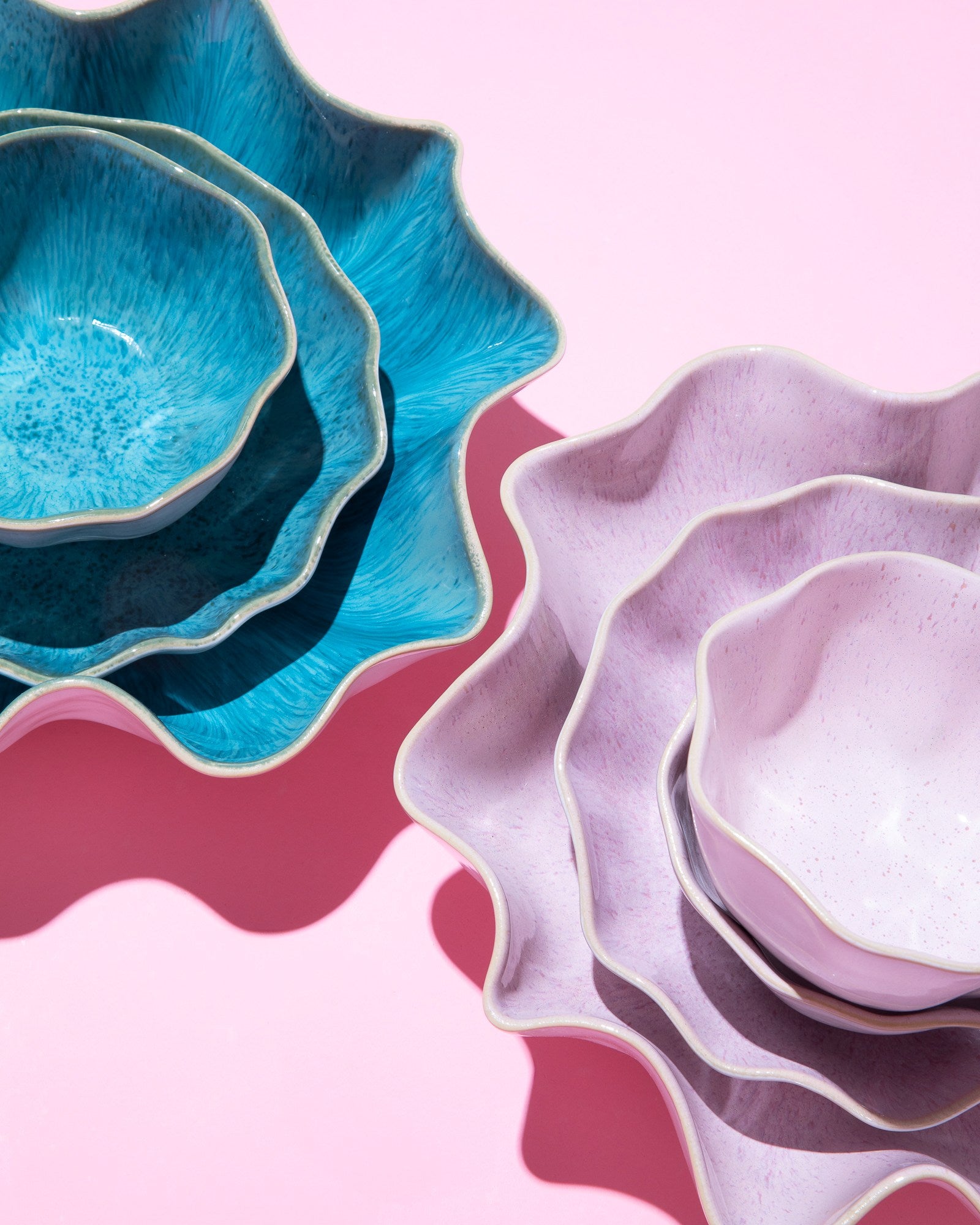 Blau und lila geschwungene Keramikteller auf rosa Hintergrund, mit ineinander liegenden Größen.