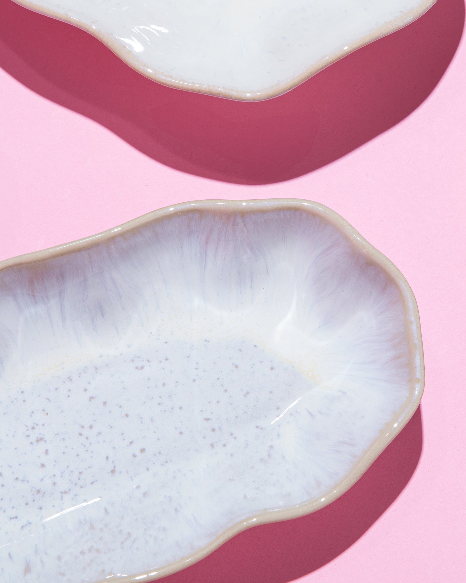 Zwei weiße, wellenförmige Keramikschalen auf einem rosa Hintergrund.