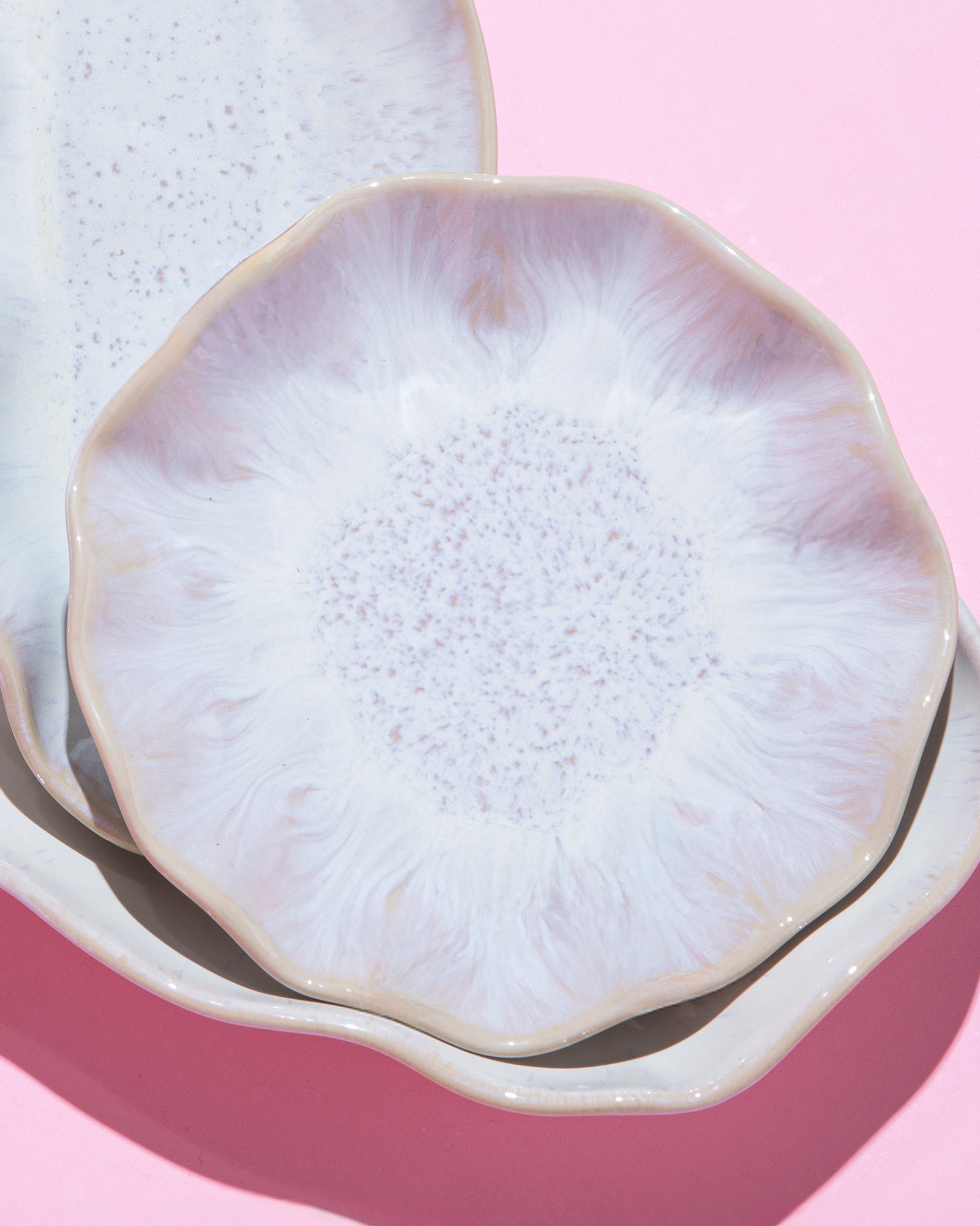 Zwei keramikähnliche Teller mit welligem Rand auf rosa Hintergrund, ineinander gestapelt und von oben fotografiert.