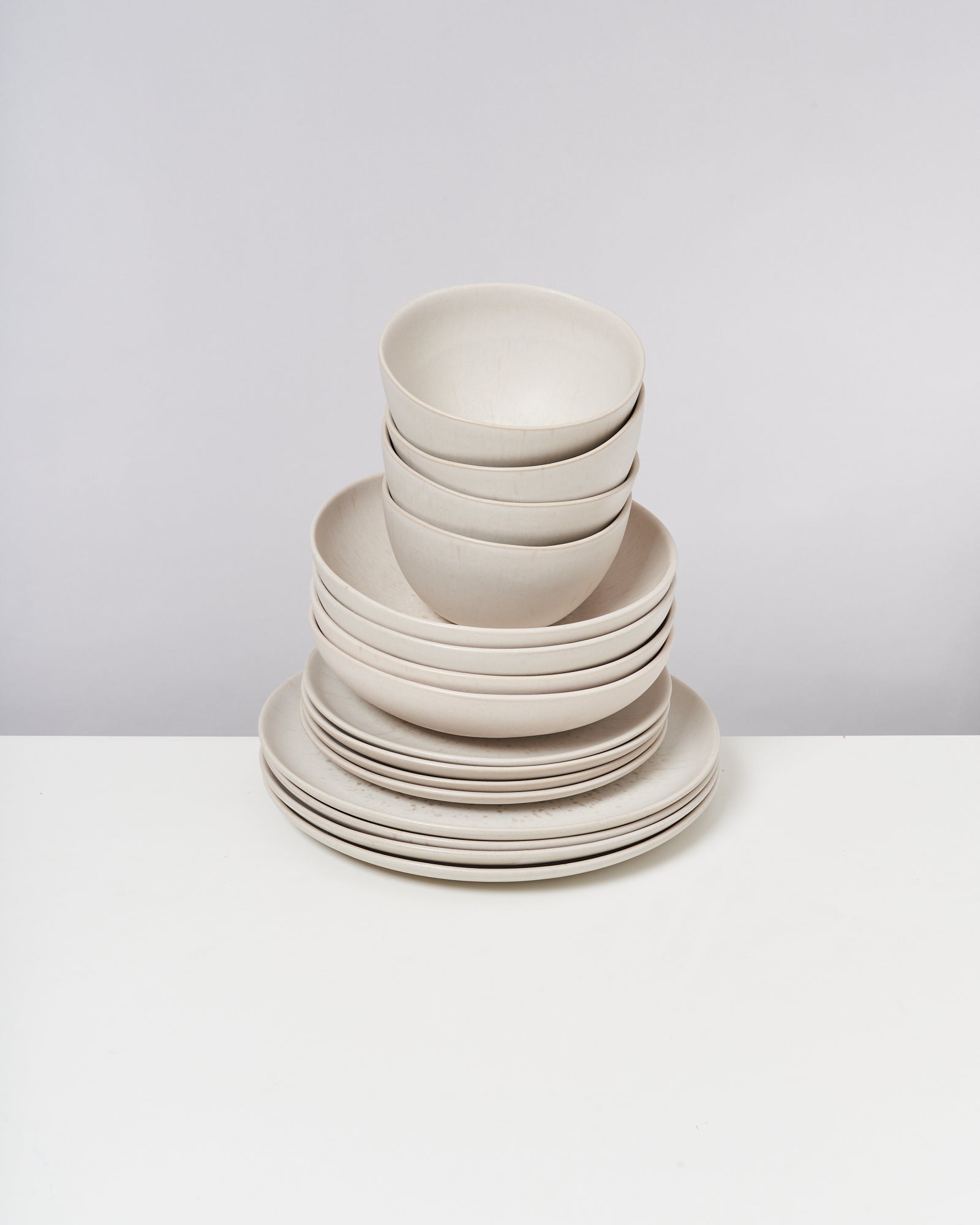 Ein Stapel weißer Schalen und Teller befindet sich auf einem weißen Tisch vor einem grauen Hintergrund.
