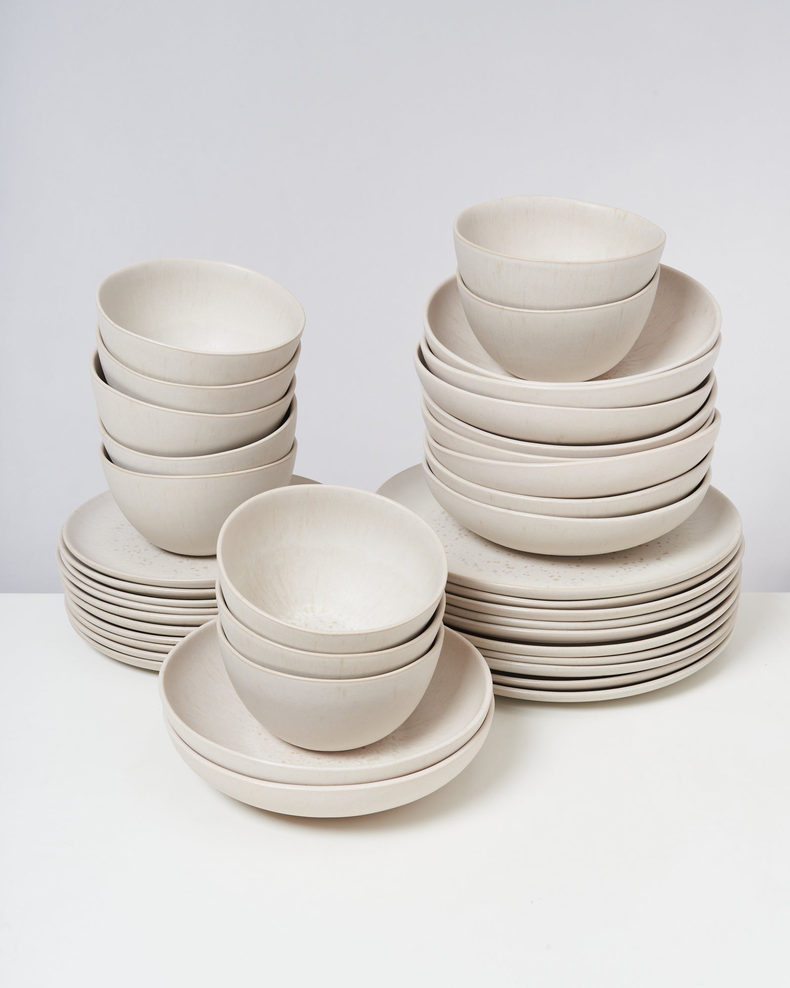 Mehrere Stapel weißer Keramikschalen und -teller auf einem weißen Tisch.