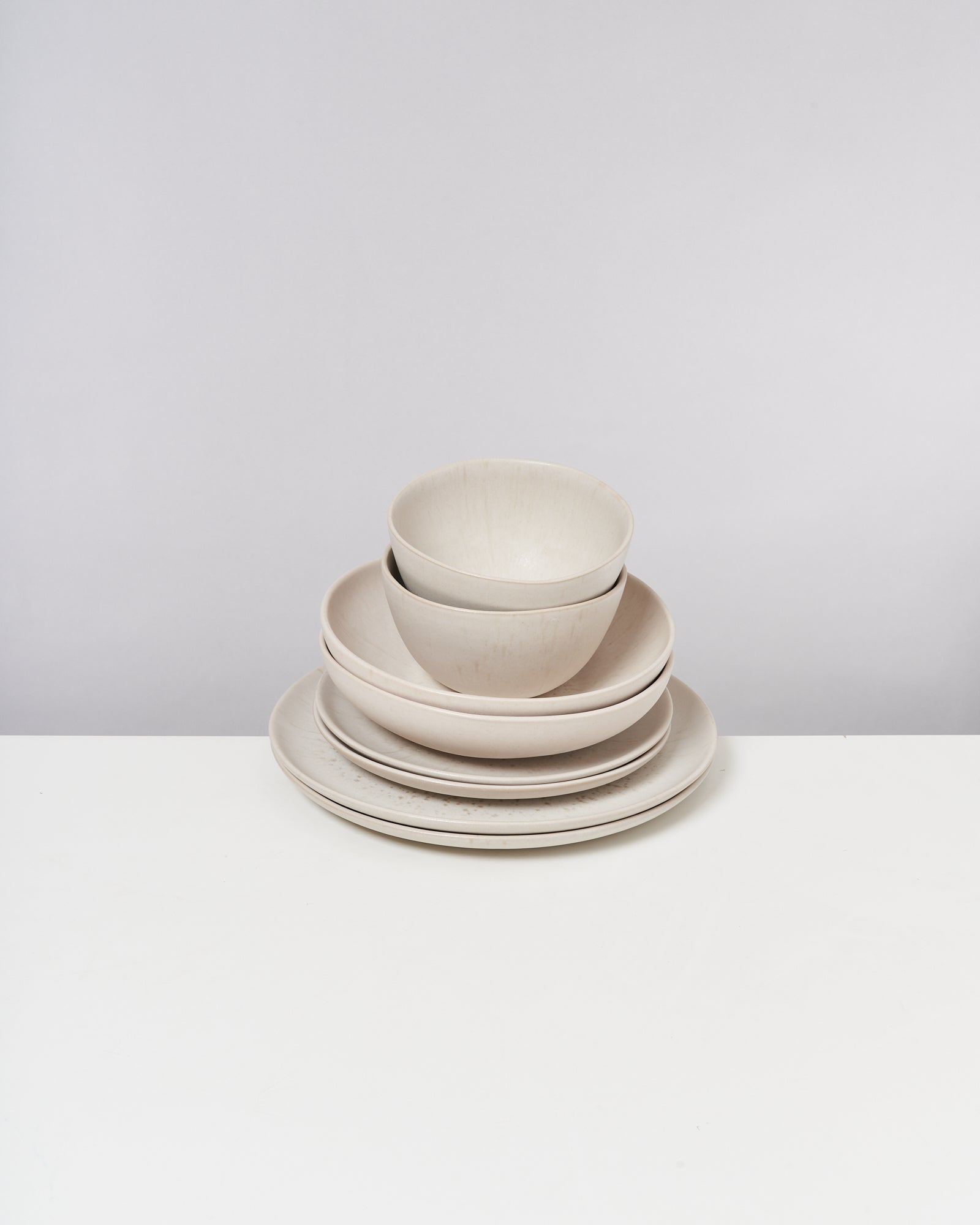 Ein Stapel aus hellen, schlichten Schüsseln und Tellern steht auf einem weißen Tisch.