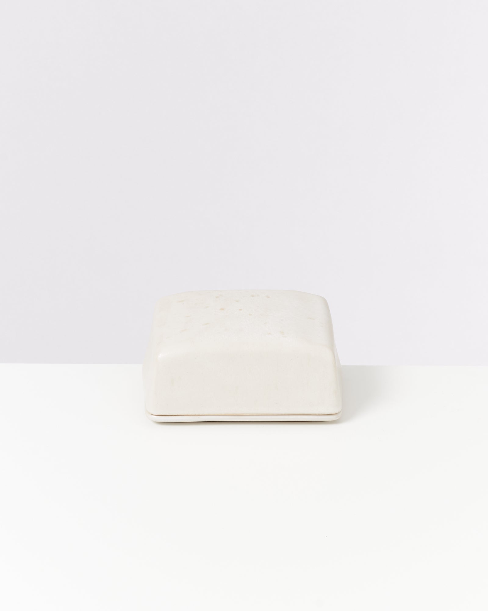 Ein weißes, quadratisches Objekt liegt auf einem weißen Untergrund vor einem weißen Hintergrund.
