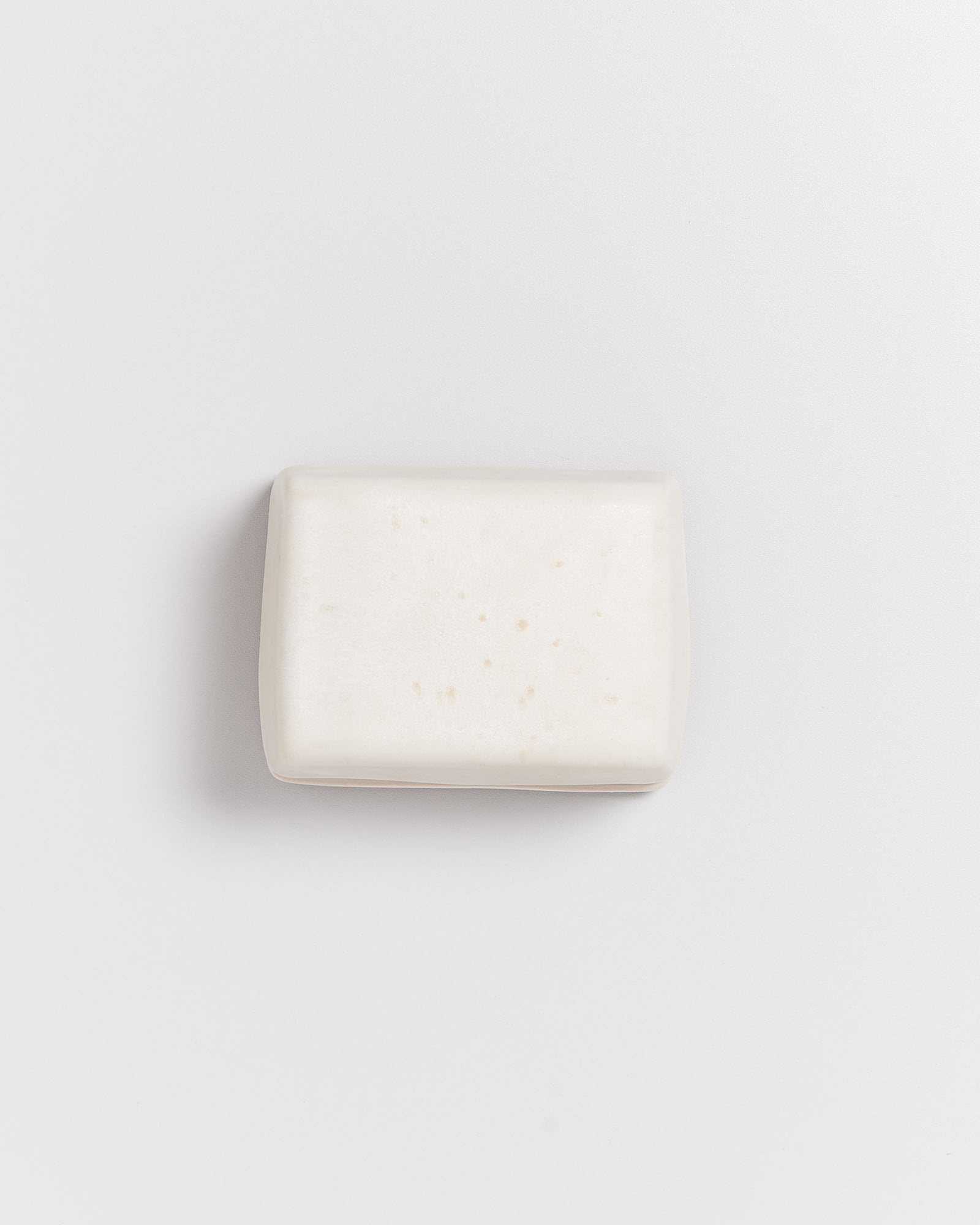 Ein rechteckiges Stück weiße Seife liegt auf einem weißen Hintergrund.