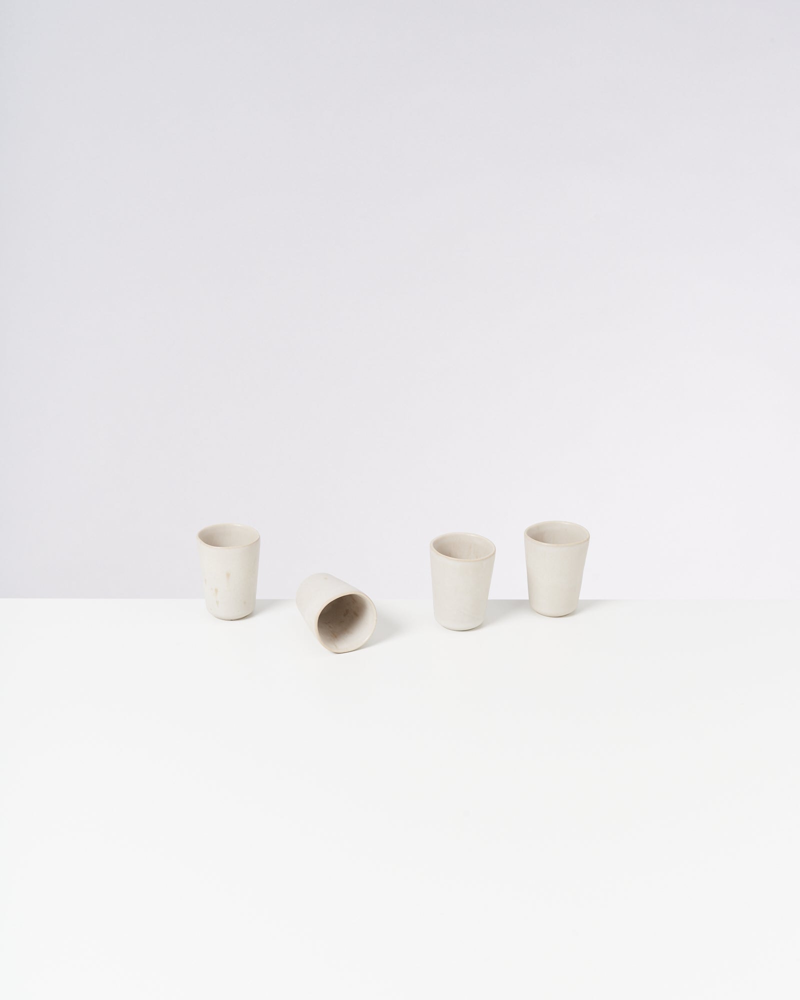 Vier weiße Becher stehen auf einem hellen Tisch, einer liegt umgekippt.