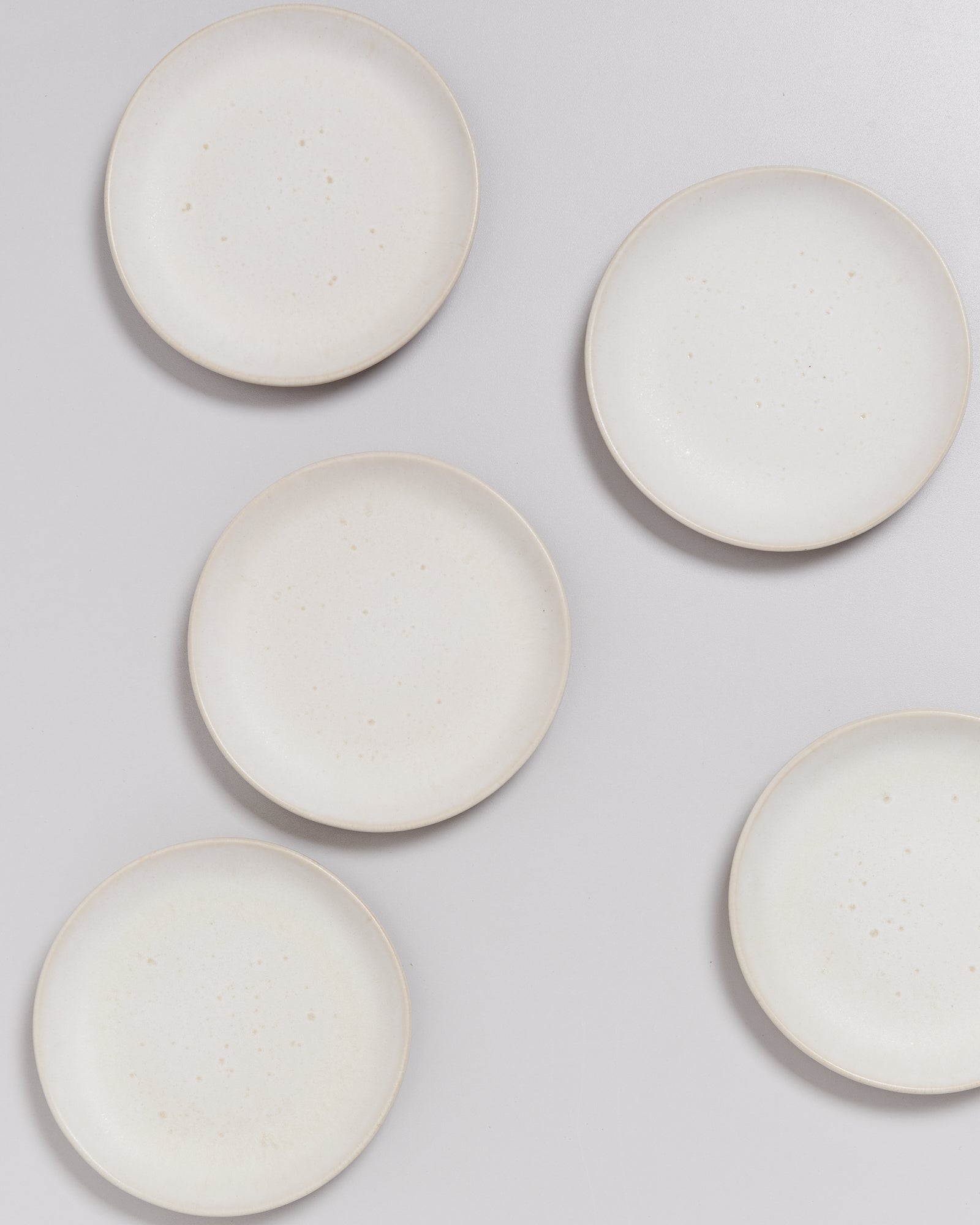 Fünf weiße Teller liegen auf einem hellgrauen Hintergrund.