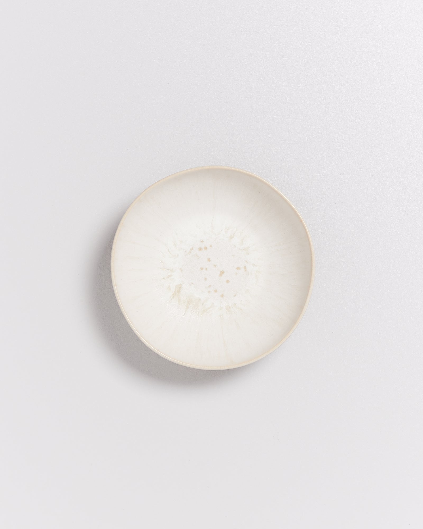 Weiße, runde Keramikschale mit feinen, braunen Sprenkeln auf einem hellen Hintergrund.