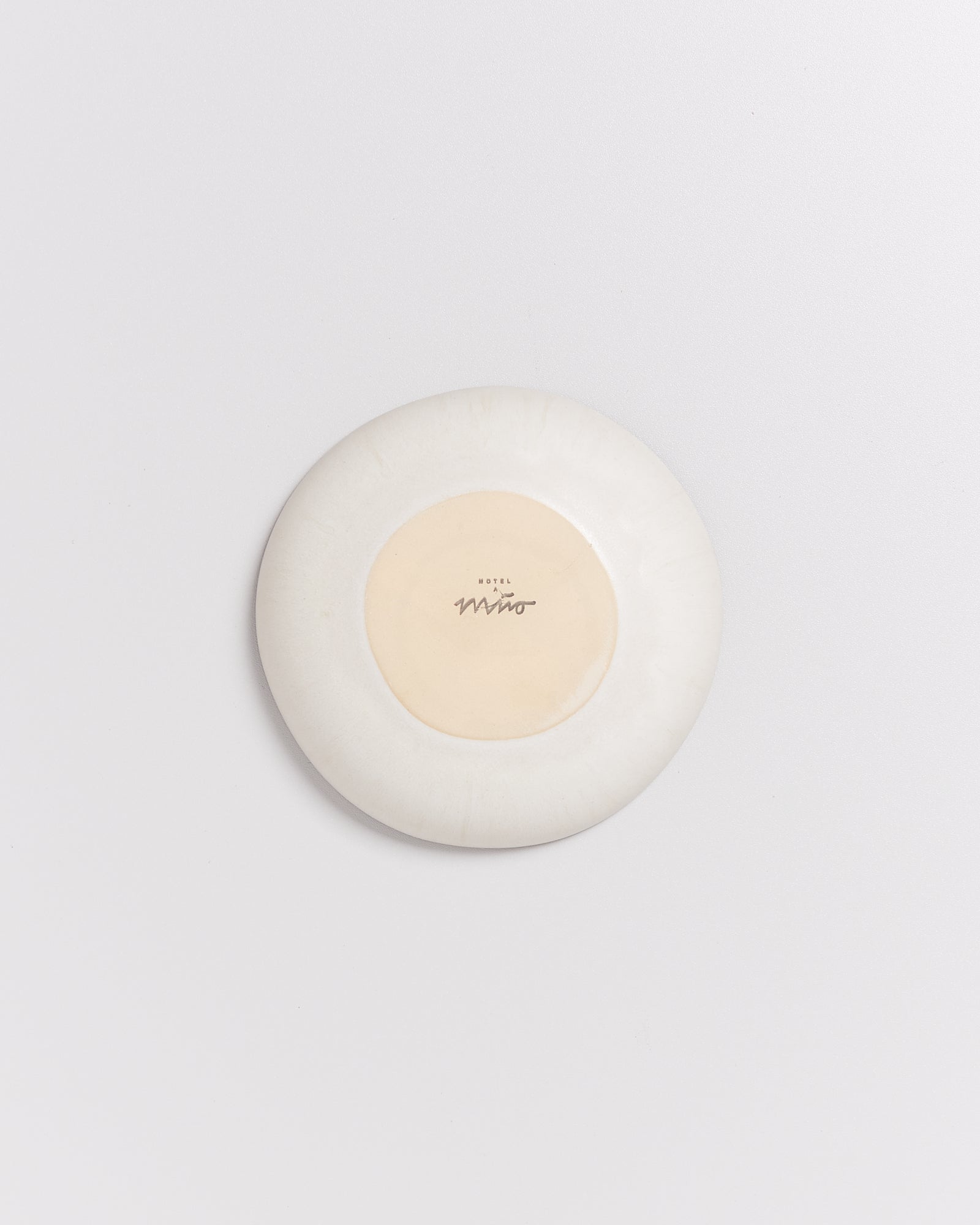 Weiße Keramikschale mit einem sandfarbenen Kreis und der Aufschrift "Hotel Miro" in der Mitte auf weißem Hintergrund.