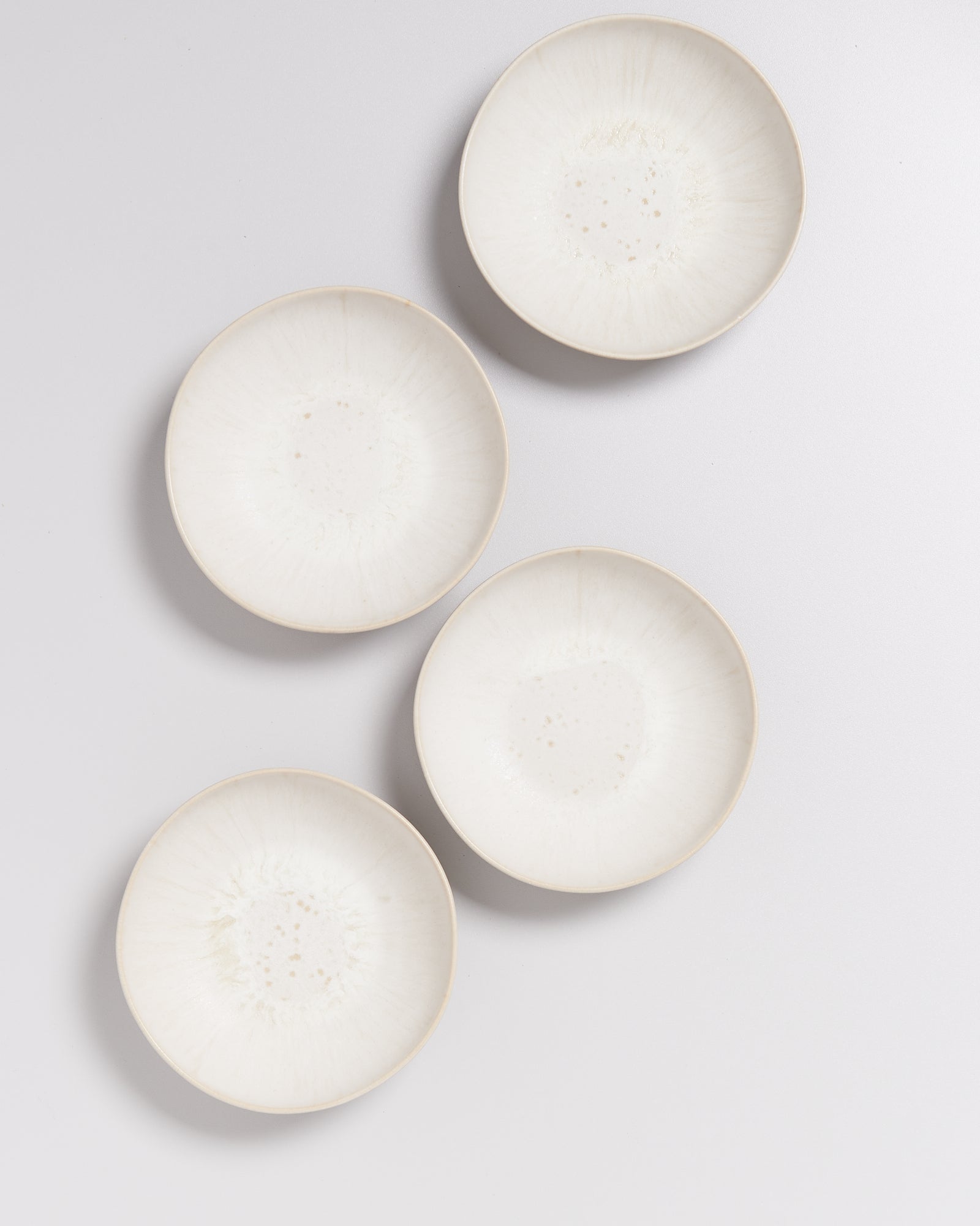 Vier weiße, runde Keramikteller sind auf einem hellen Hintergrund angeordnet.