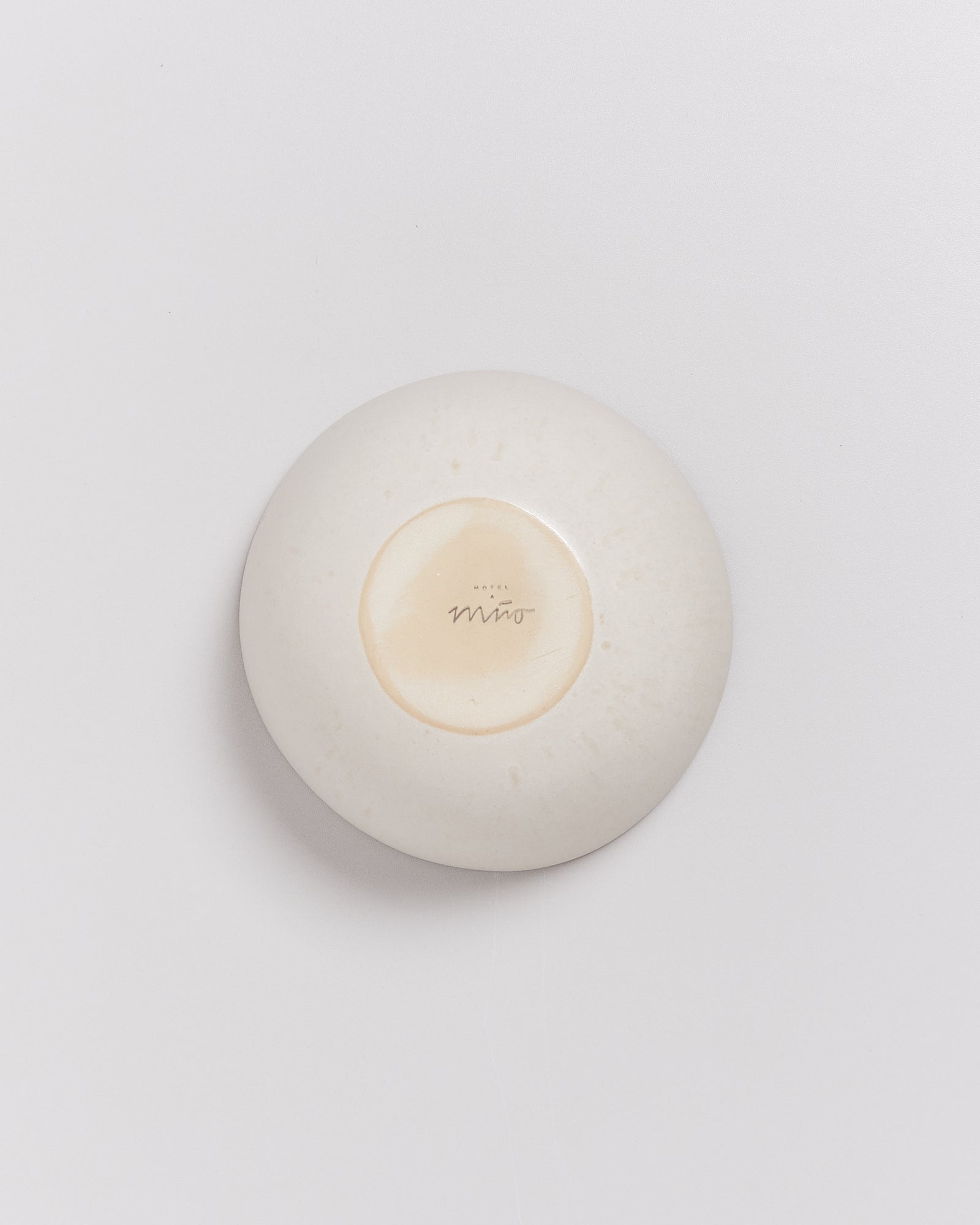 Runde, beigefarbene Seifenschale mit Schriftzug "Hotel Miro" auf der Unterseite, auf weißem Hintergrund.