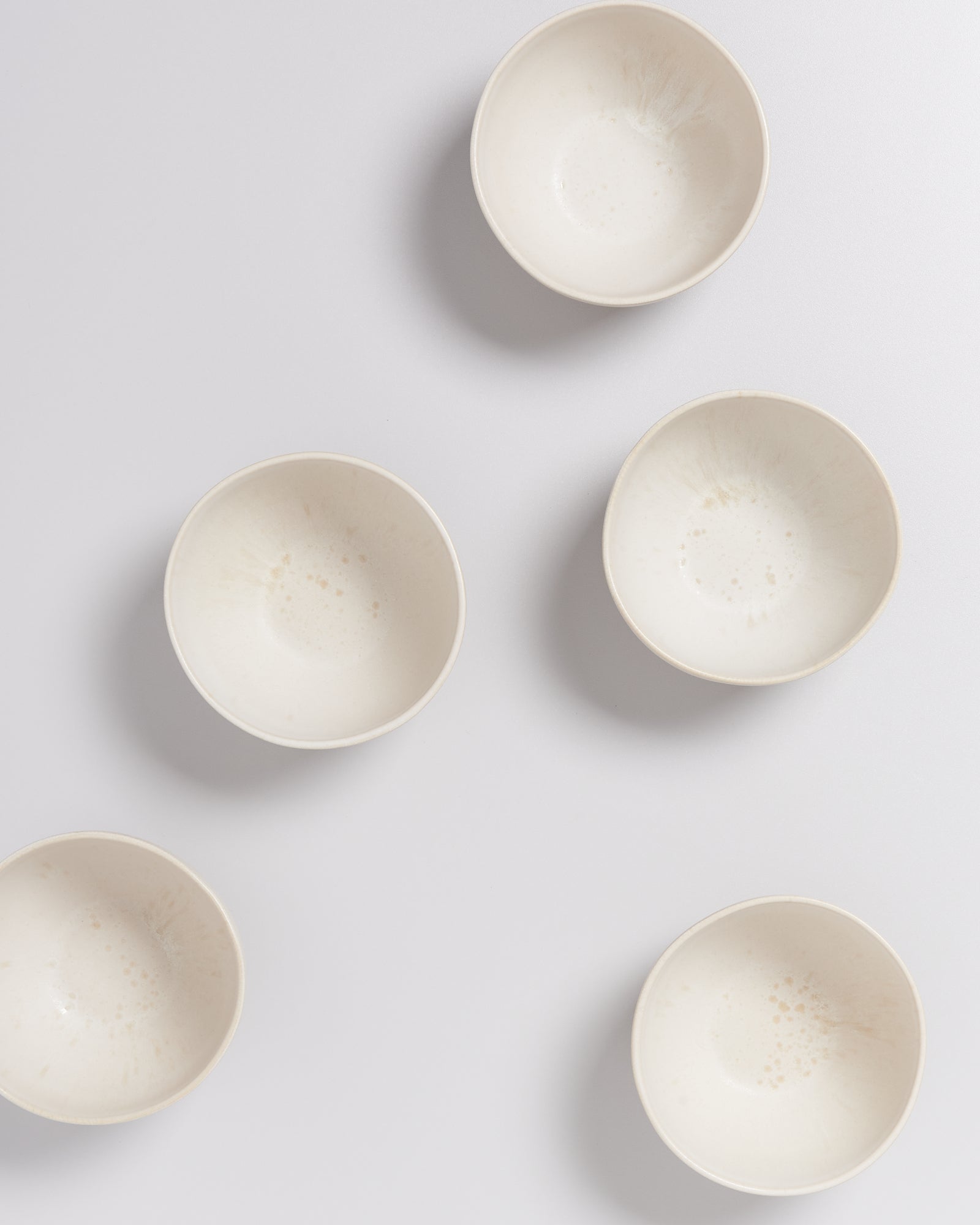 Fünf cremefarbene Schalen auf einem weißen Hintergrund, gleichmäßig verteilt.