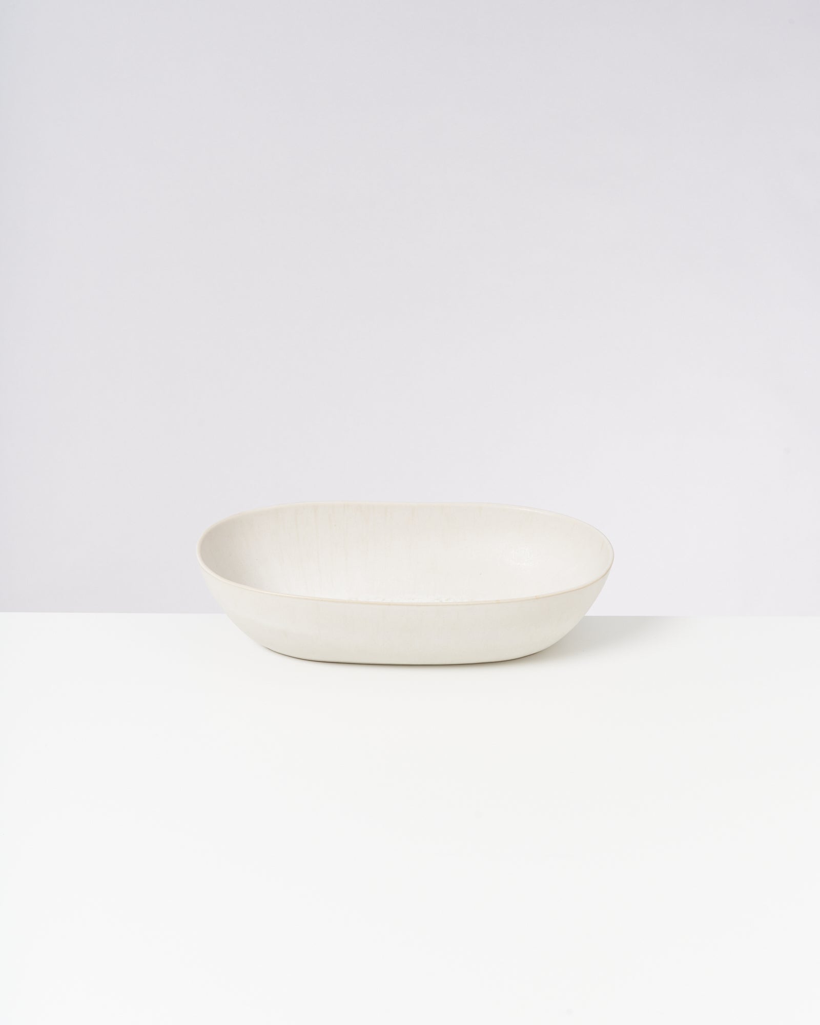 Ovale, cremefarbene Keramikschale steht auf einem weißen Hintergrund.