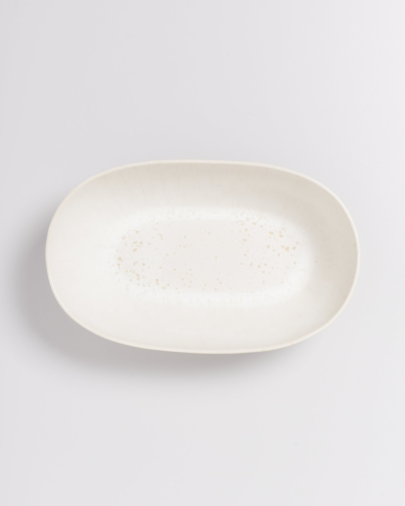 Ovaler, weißer Keramikteller mit feiner Sprenkelung auf einer hellen Oberfläche.