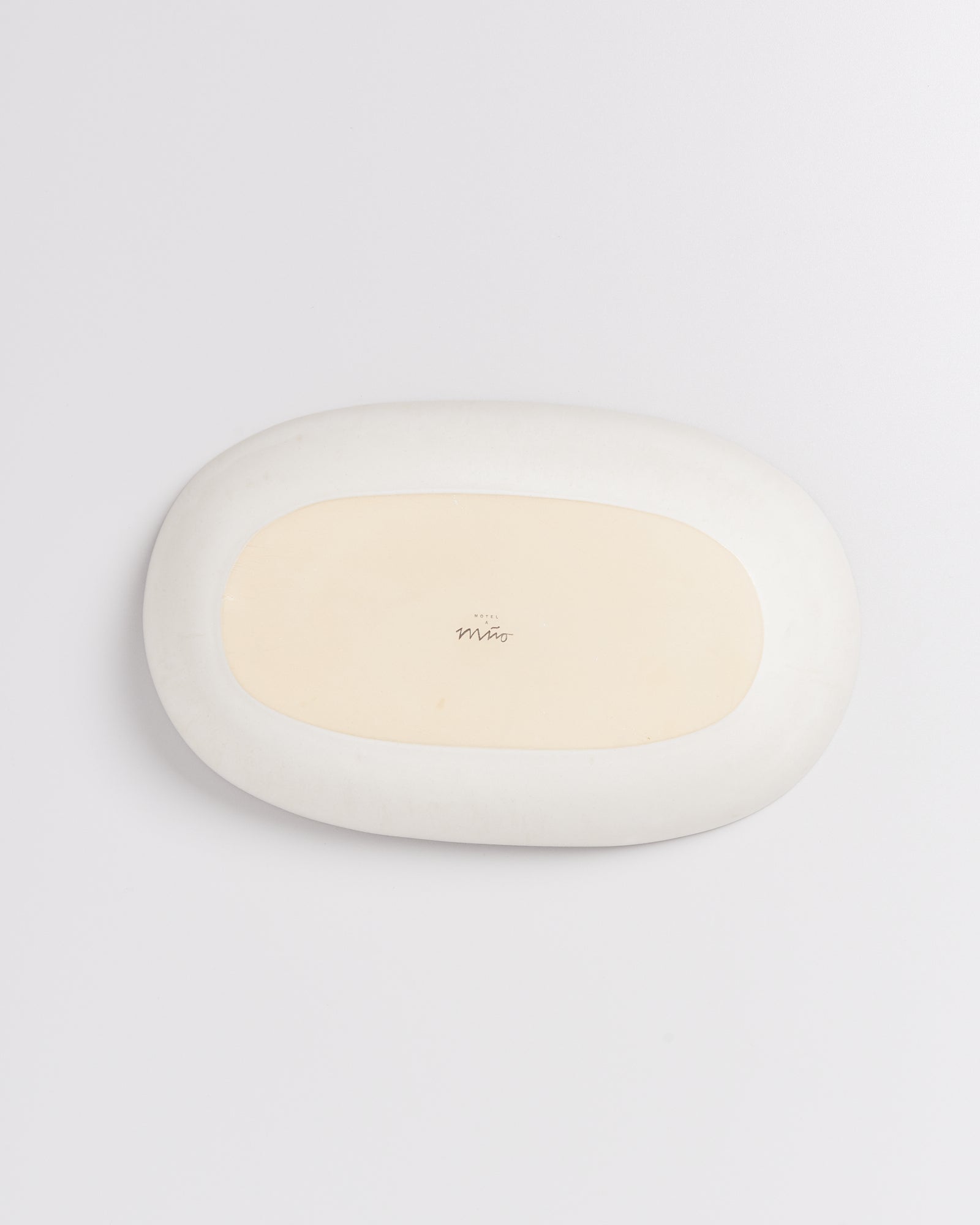 Weiße, ovale Keramikplatte mit beigem Zentrum und kleiner Aufschrift in der Mitte, auf weißem Hintergrund.