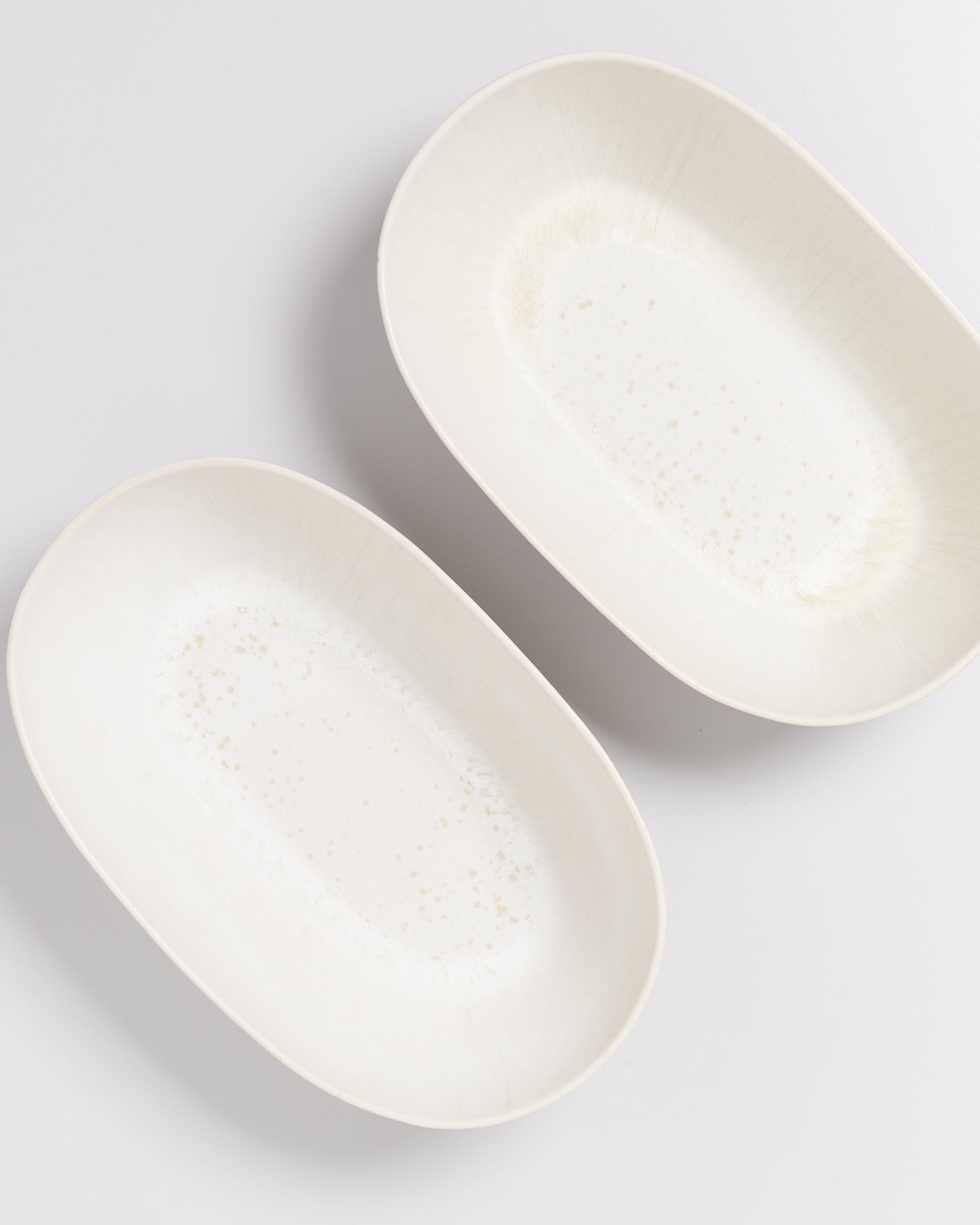 Zwei ovale, weiße Keramikteller mit dezenter Musterung auf einer weißen Oberfläche.