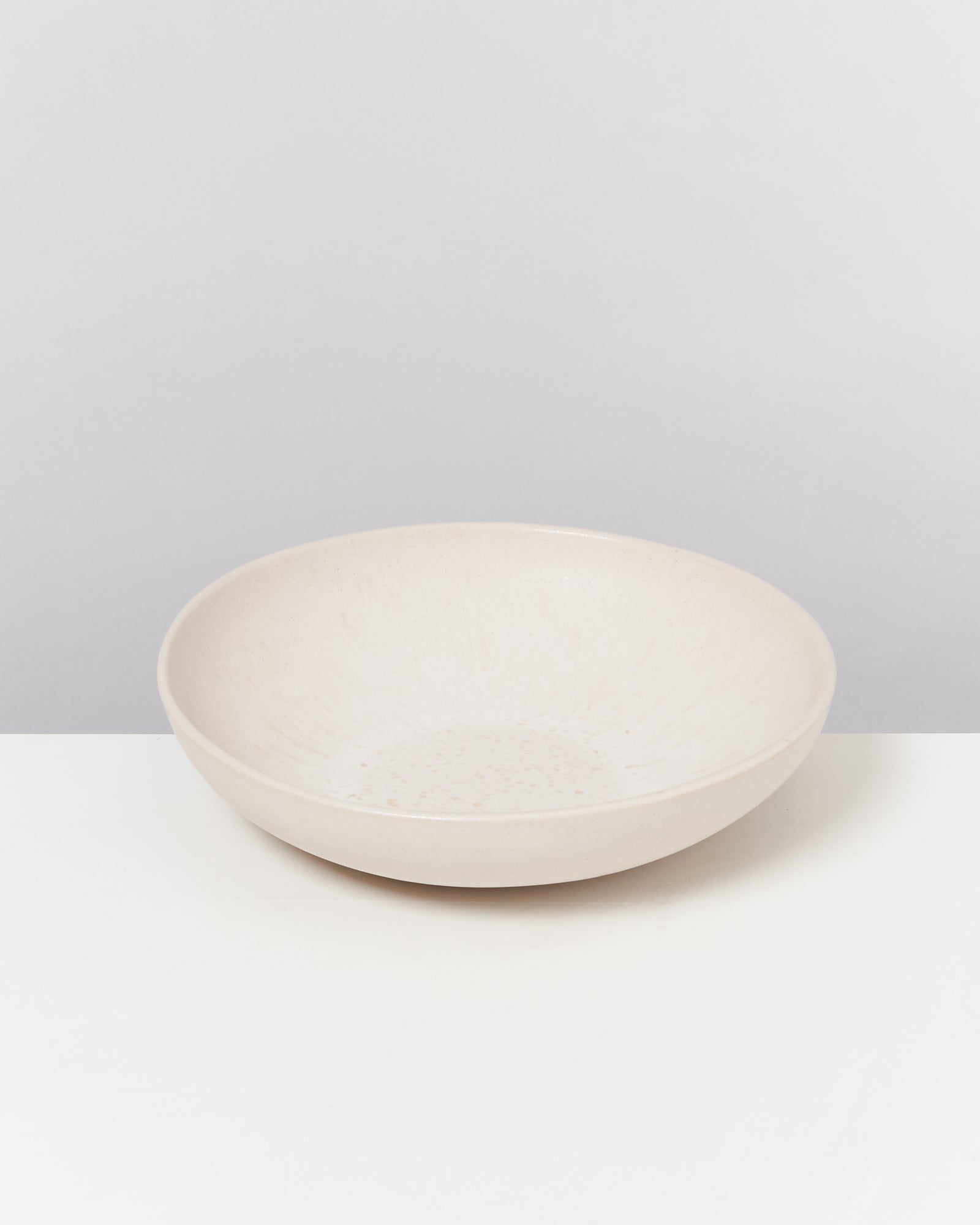 Beige, flache Keramikschale auf weißem Hintergrund.