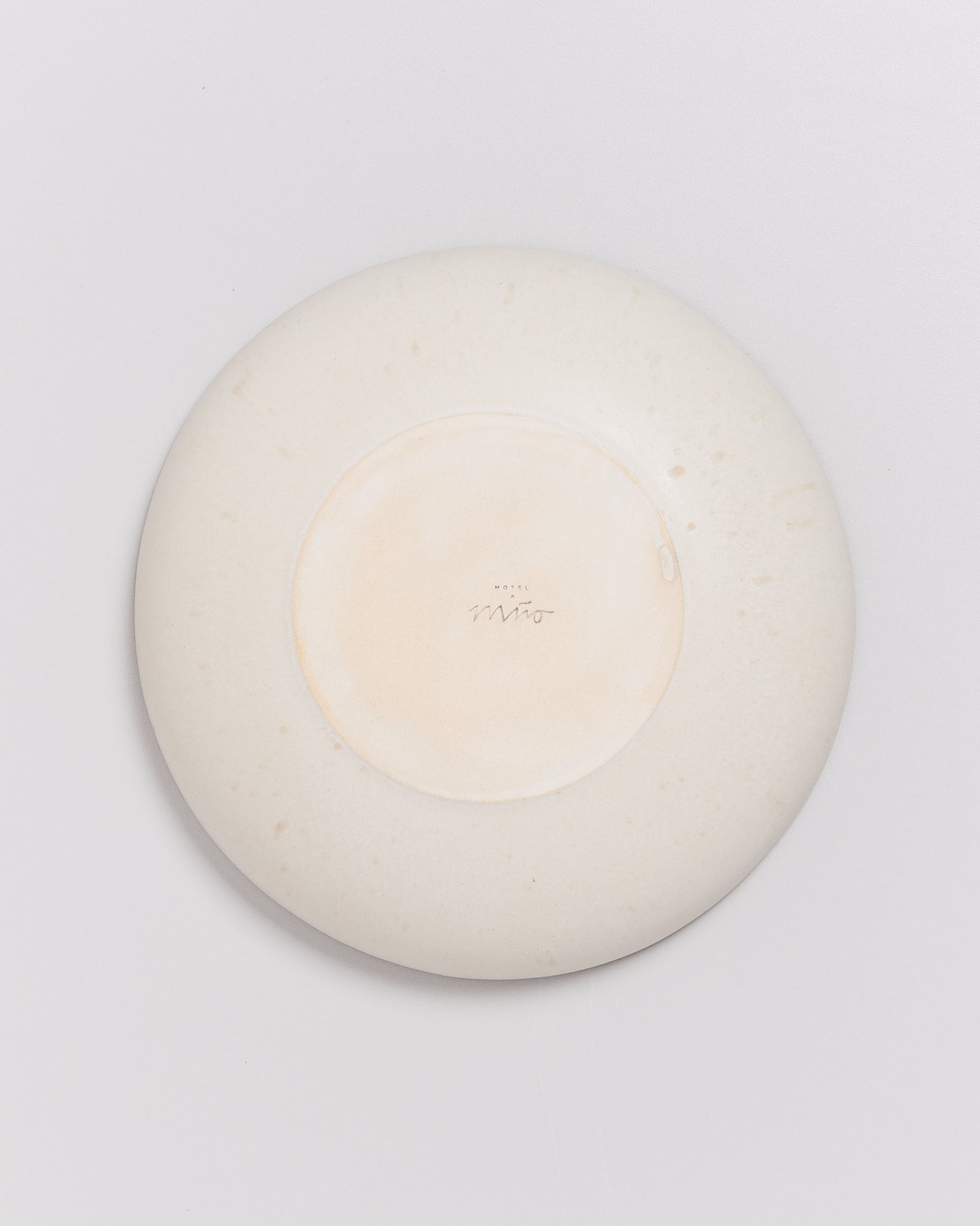 Rückseite eines weißen Tellers auf einem hellgrauen Hintergrund, mit Aufschrift undefinierbar in der Mitte.