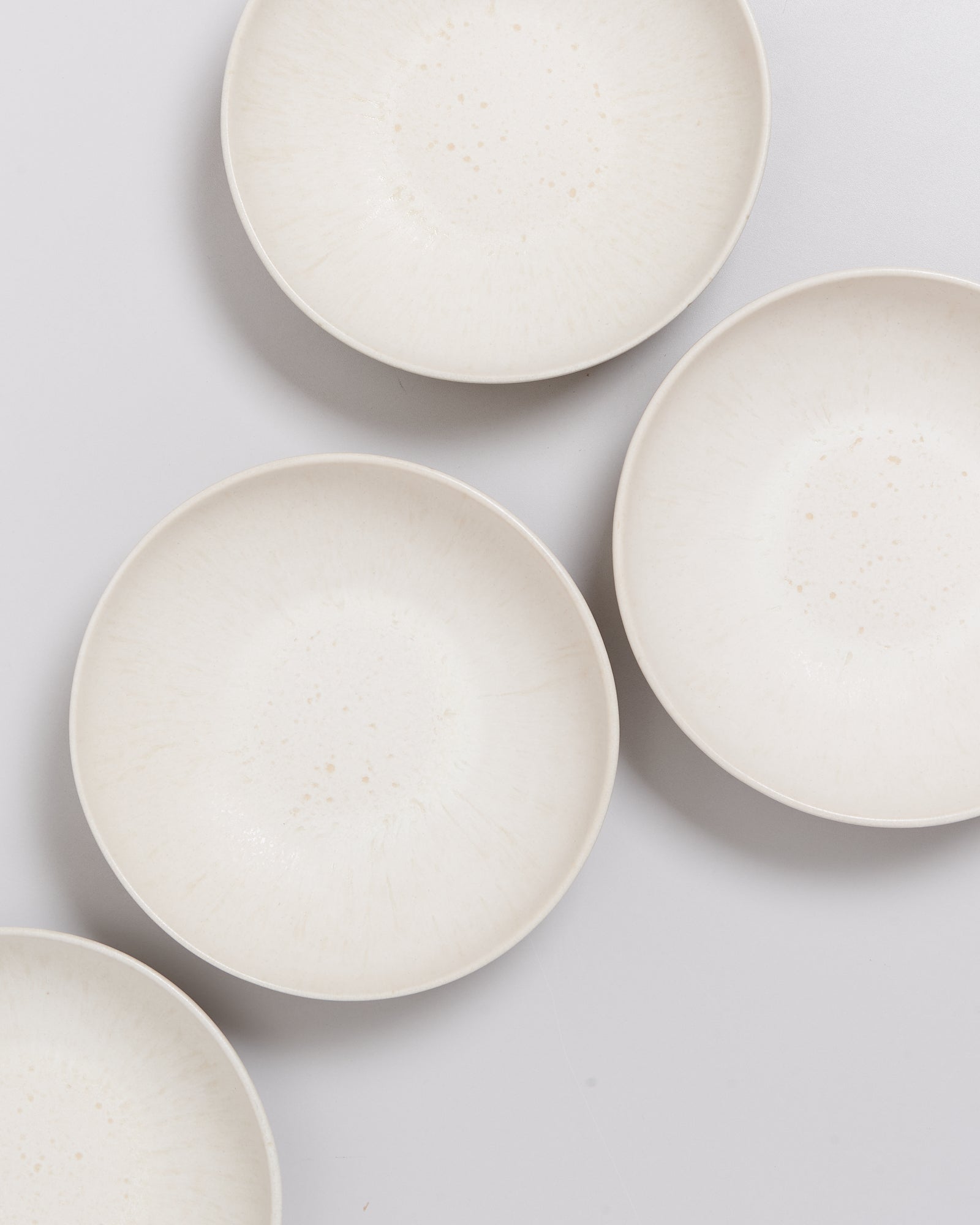 Vier weiße, flache Teller auf einem hellen Hintergrund angeordnet.