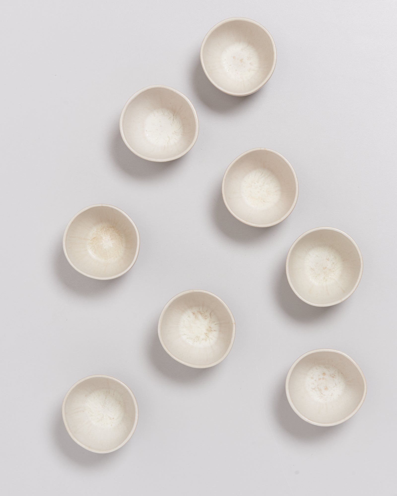 Acht leere, weiße Schalen sind auf einer grauen Oberfläche angeordnet.