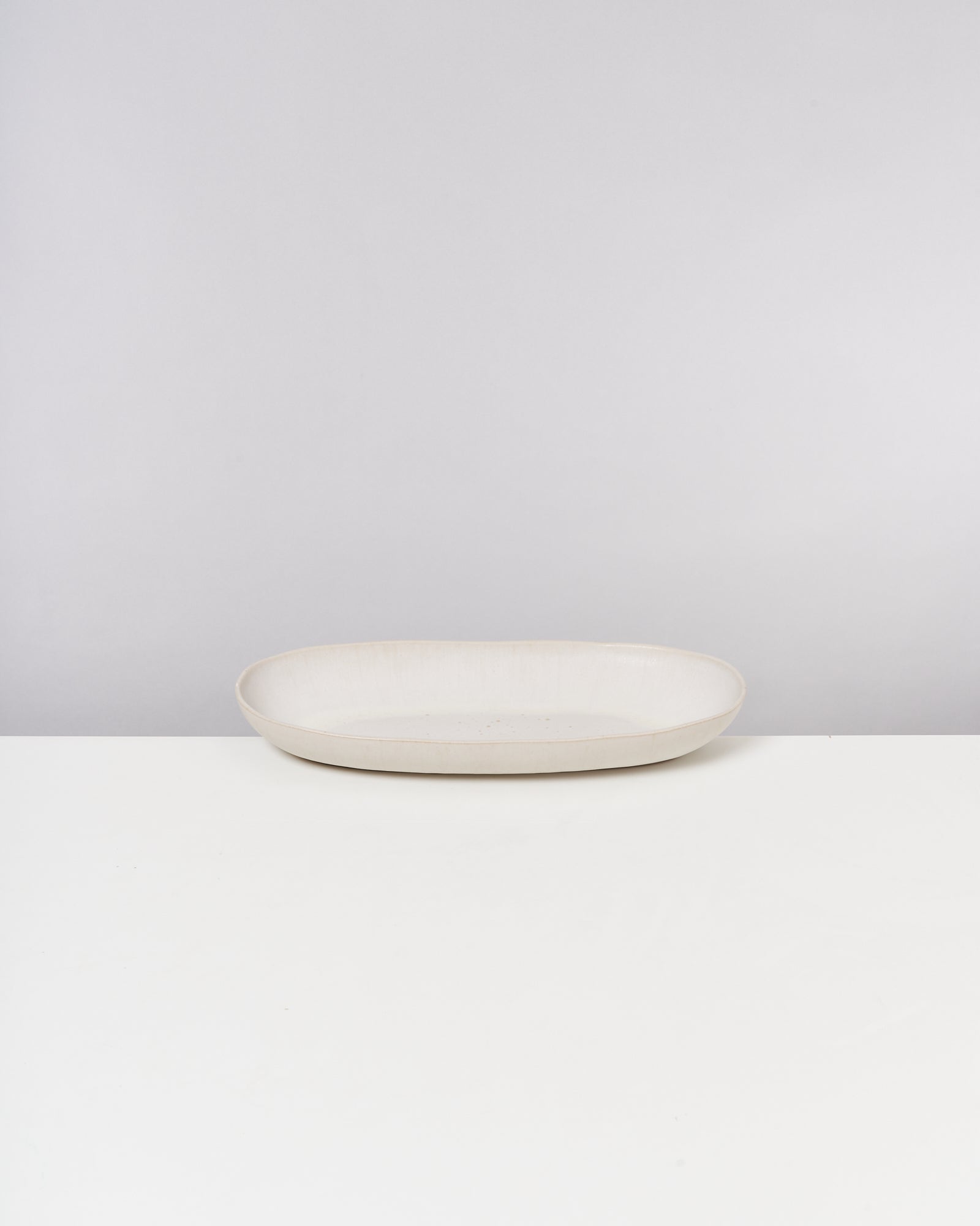 Ovaler, weißer Keramikteller auf einem weißen Tisch vor neutralem Hintergrund.