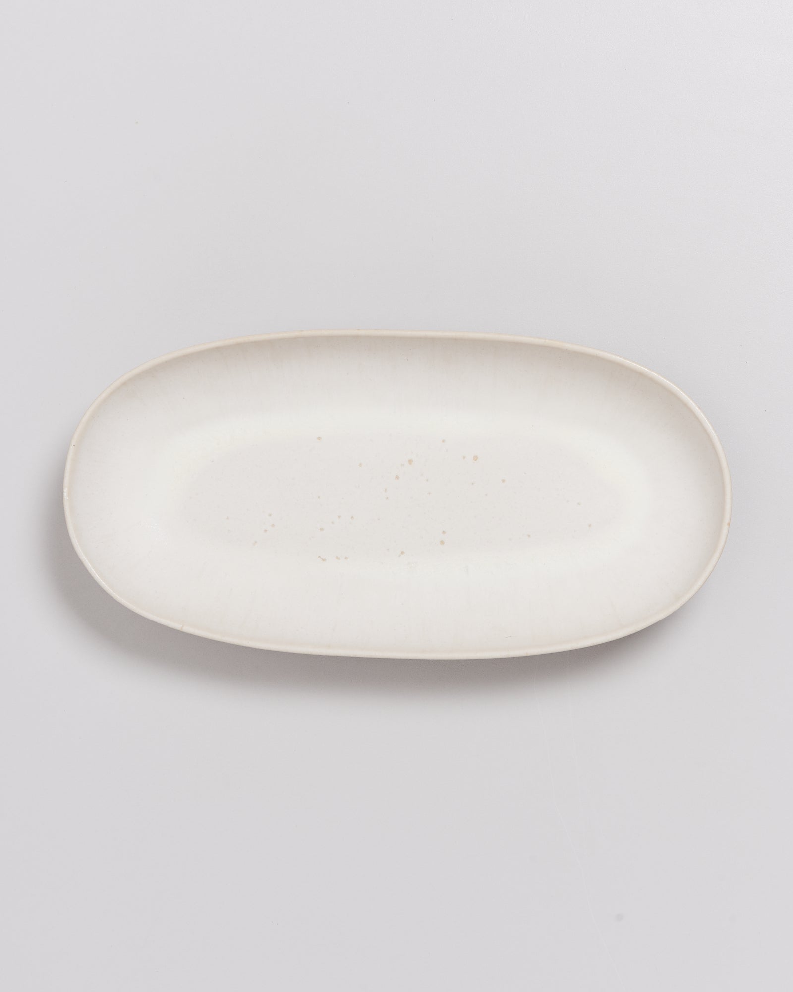Beiger, ovaler Keramikteller auf hellem Hintergrund.