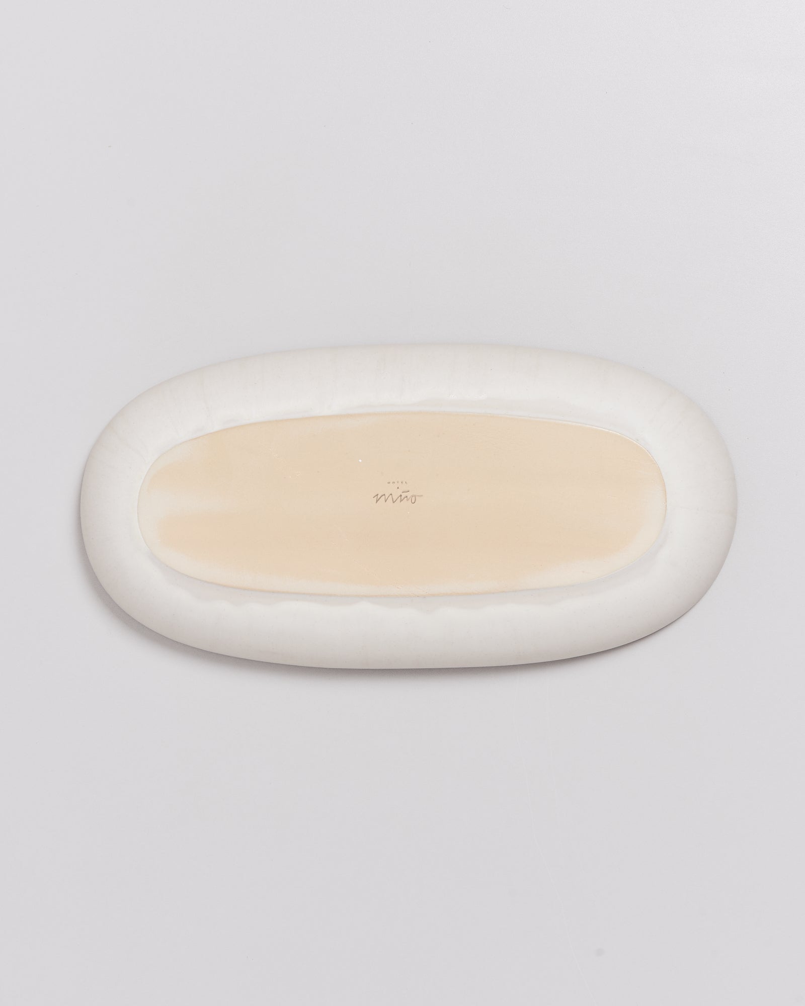 Ein ovaler, cremefarbener Teller mit einer weißen Umrandung auf einem weißen Hintergrund.