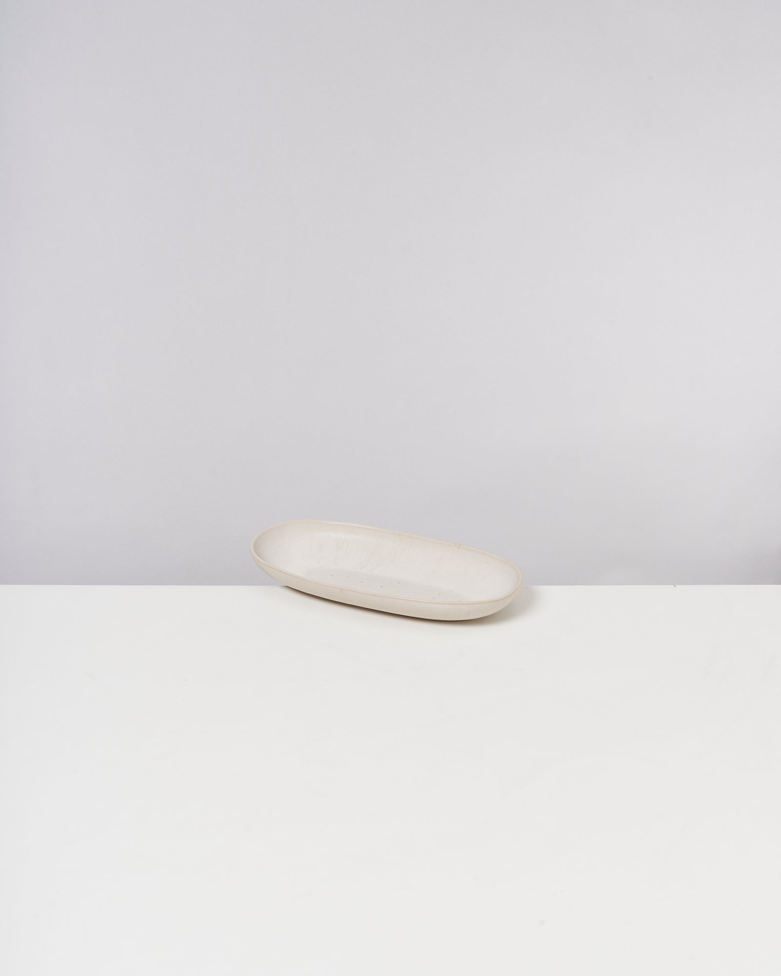 Beigefarbene ovale Schale auf einem weißen Tisch vor einem hellgrauen Hintergrund.