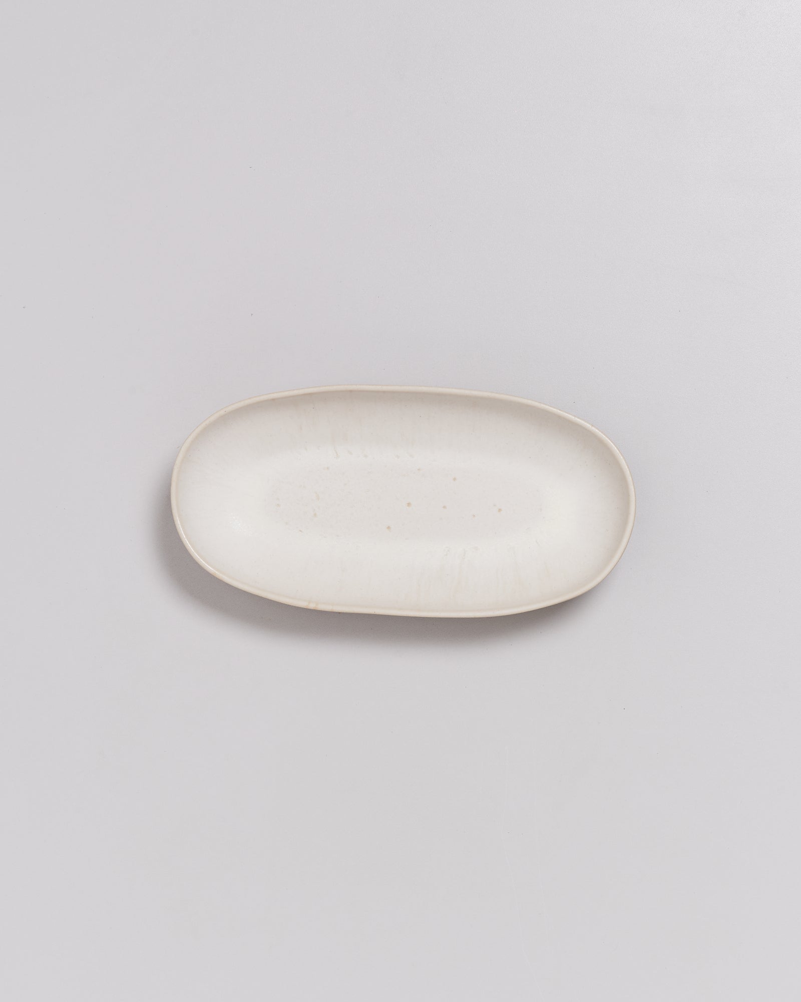 Weiße, ovale Keramikplatte auf einem grauen Hintergrund.