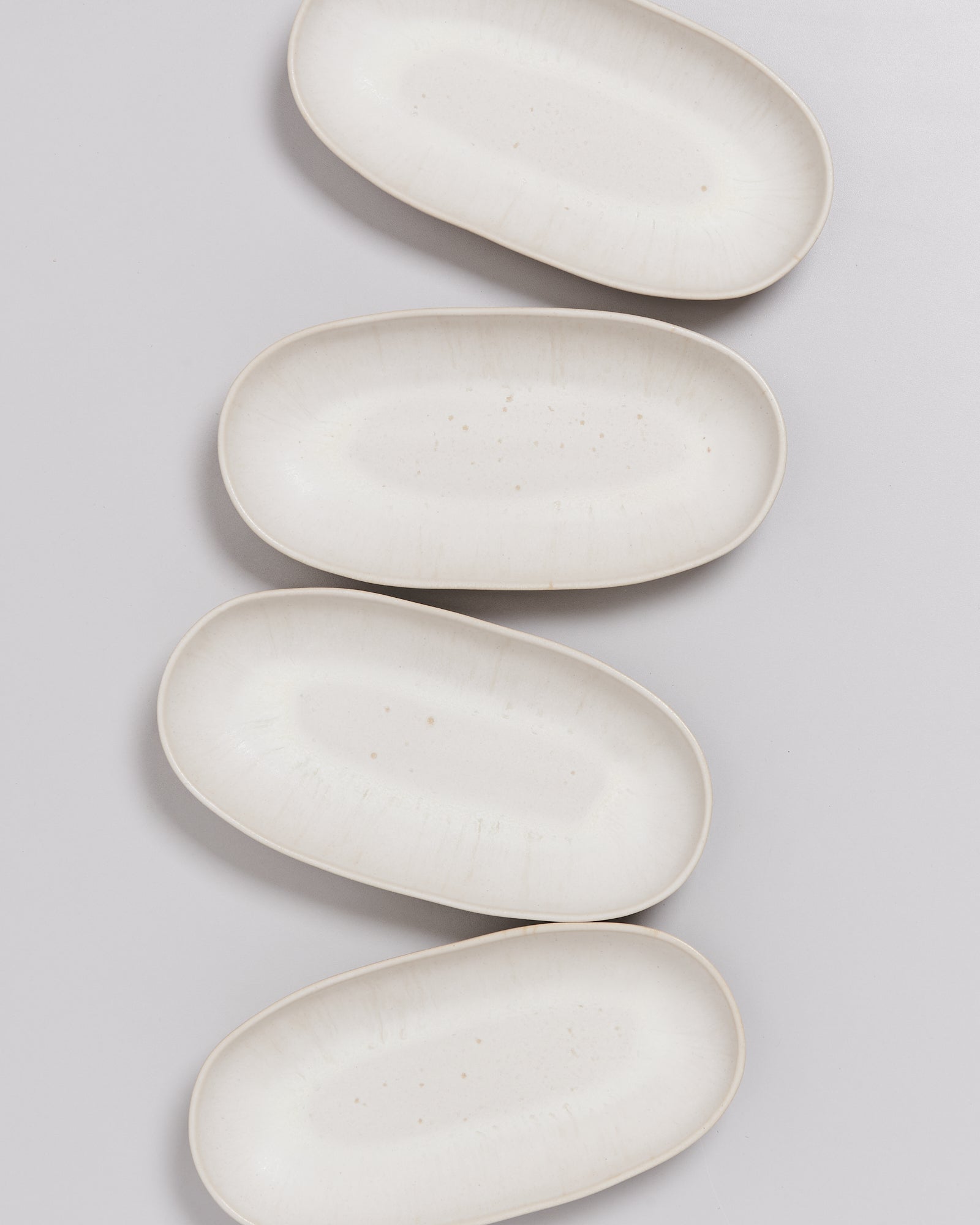 Vier weiße, ovale Teller liegen auf einem hellen Hintergrund, leicht versetzt zueinander angeordnet.