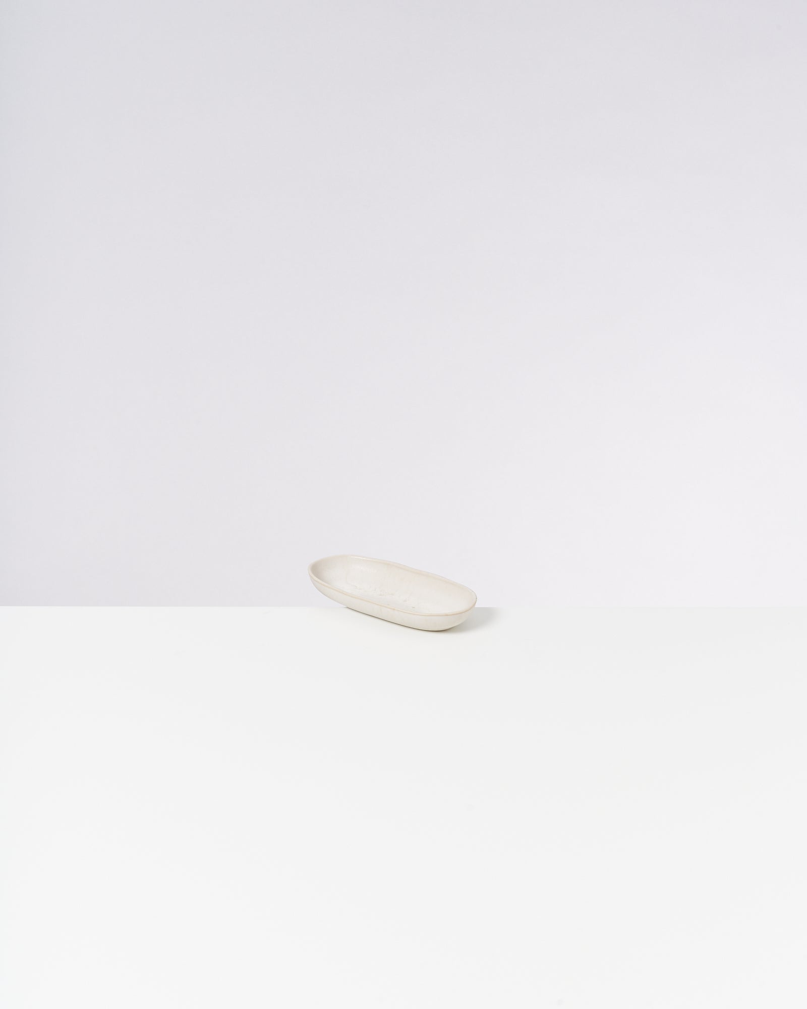 Weiße ovale Schale auf einer weißen Oberfläche vor einem hellen Hintergrund.