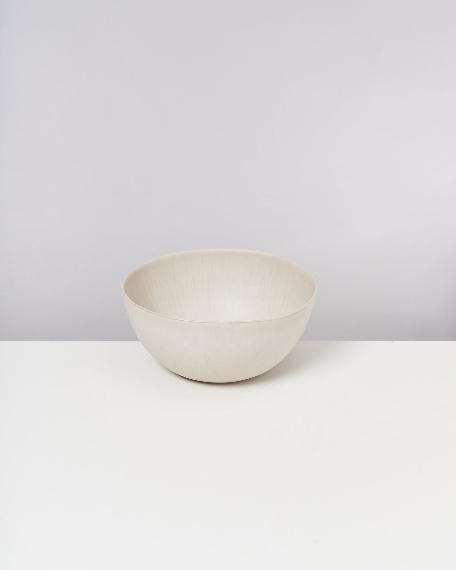 Eine cremefarbene Schale steht auf einem weißen Tisch vor einem neutralen Hintergrund.